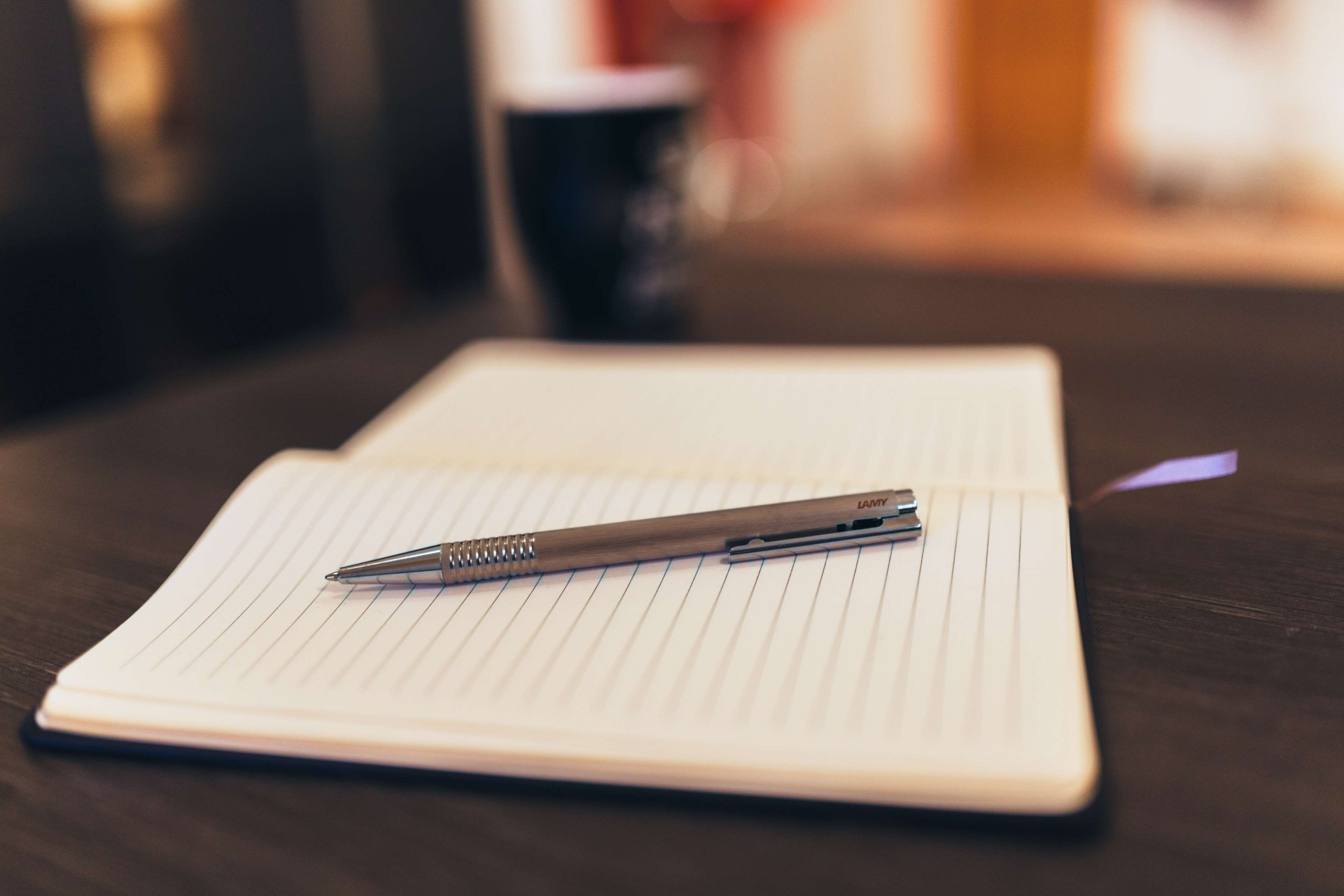 Pen on a lined notebook with a cup in the background HD Wallpaper