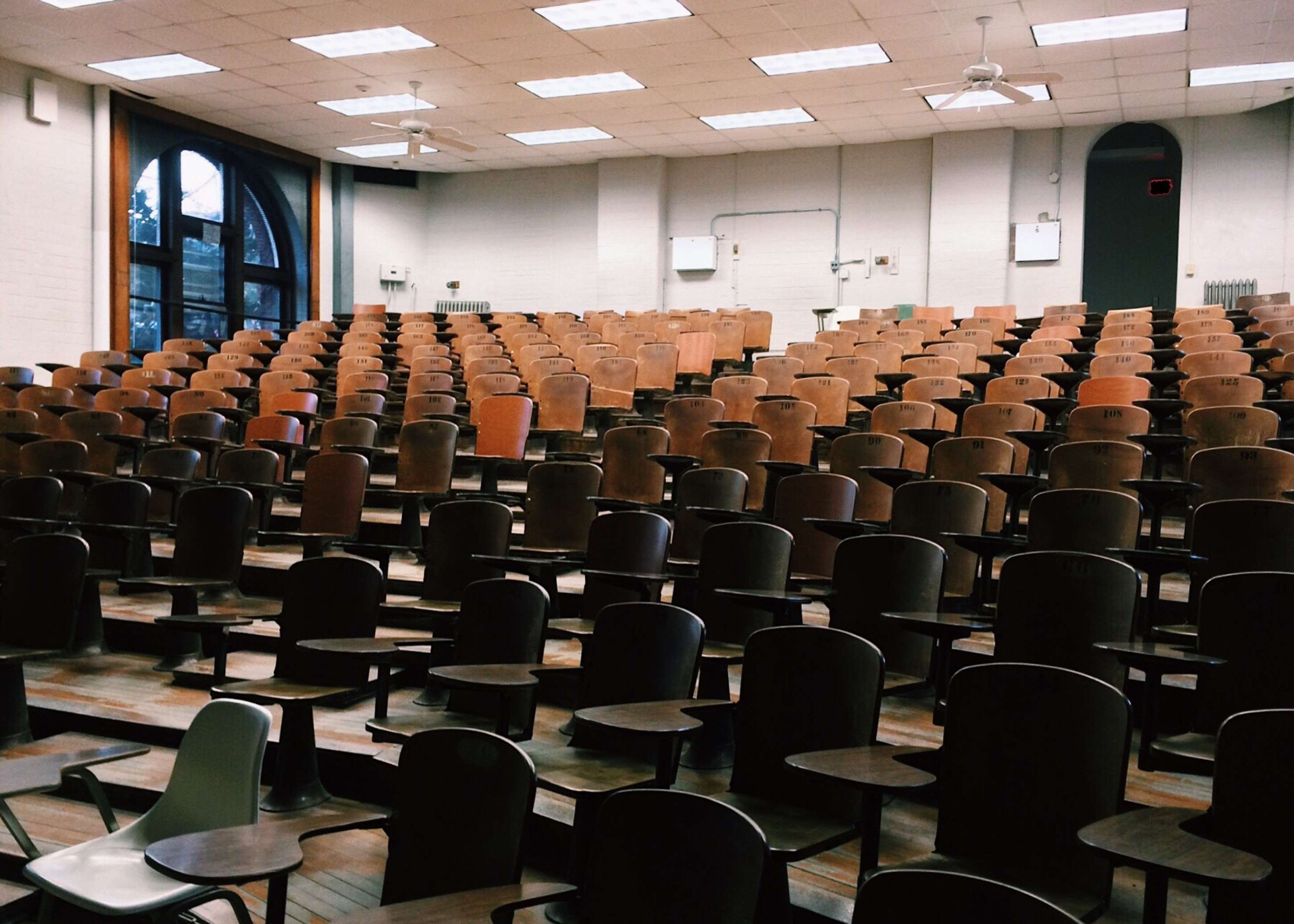 Empty lecture hall with tiered wooden seats and desks HD Wallpaper