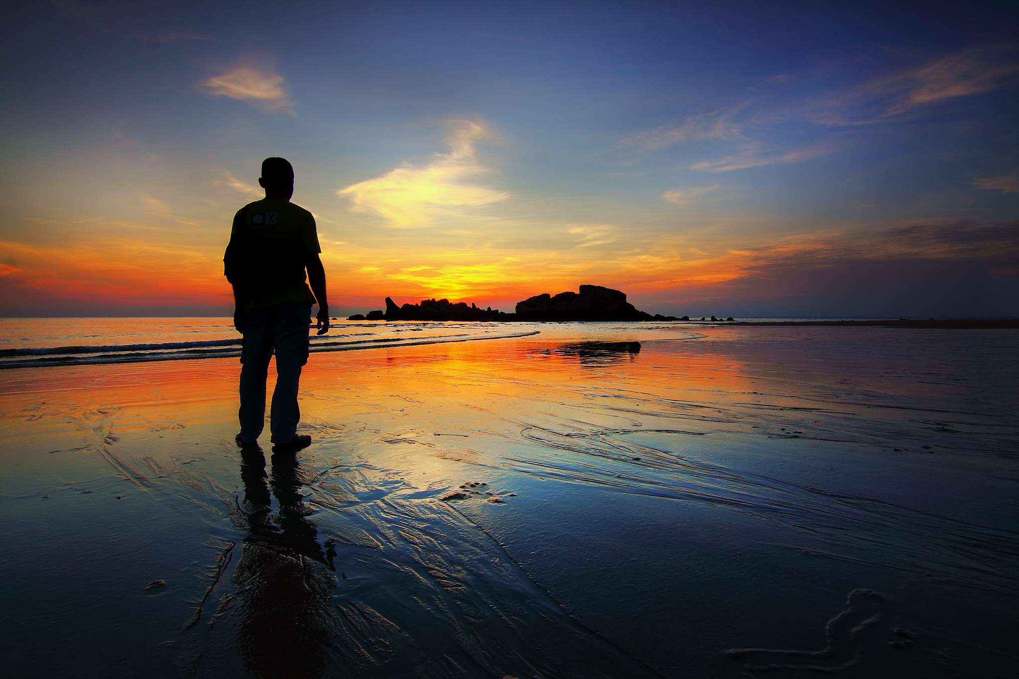 Man silhouetted on a beach at sunset HD Wallpaper