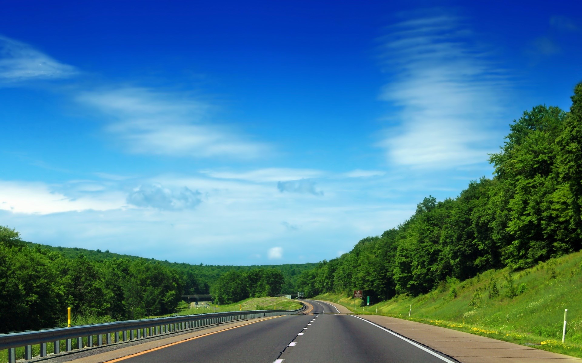 Highway through a green forest under a blue sky HD Wallpaper