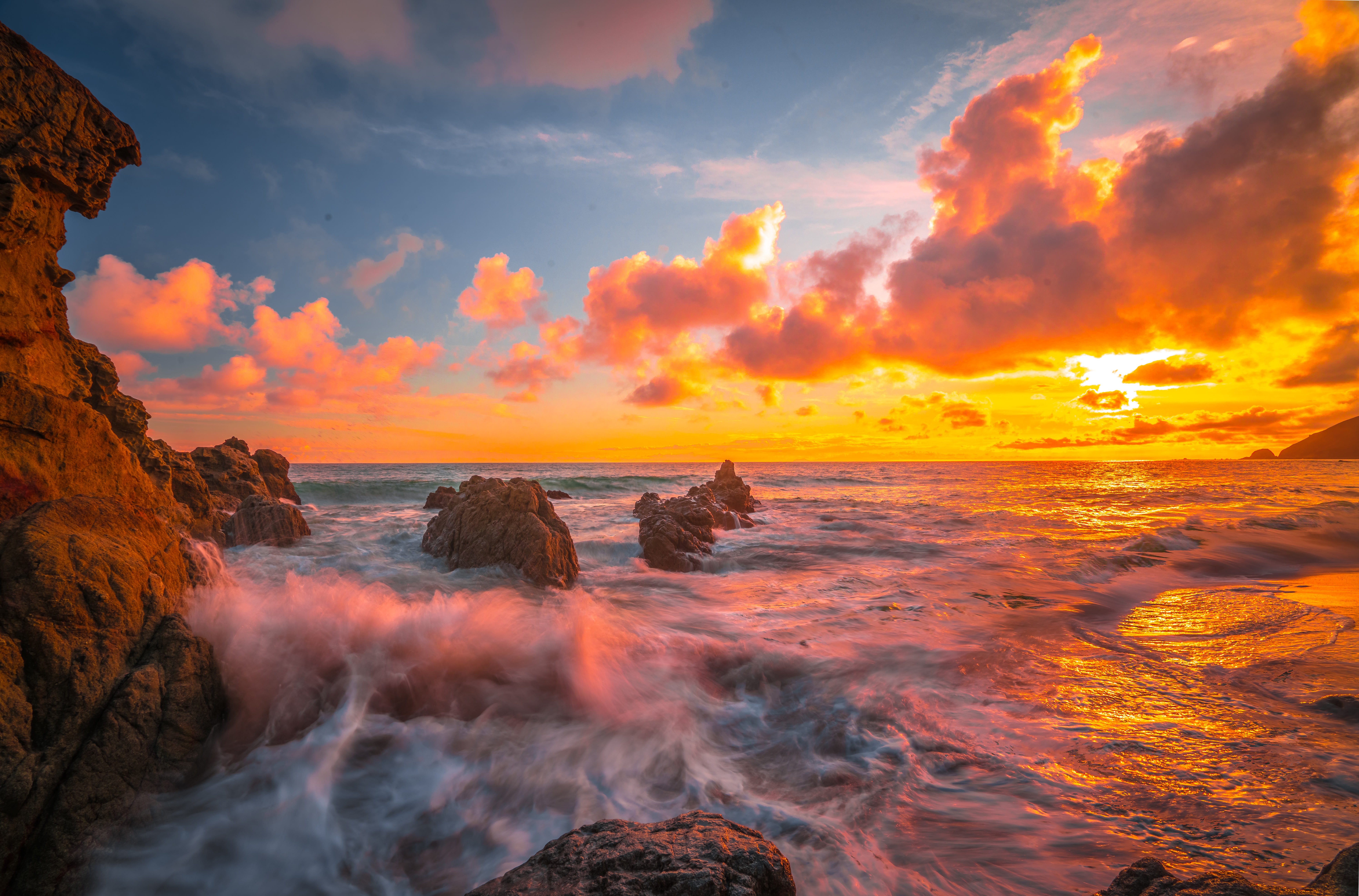 Sunset over the ocean with dramatic clouds and rocky shore HD Wallpaper