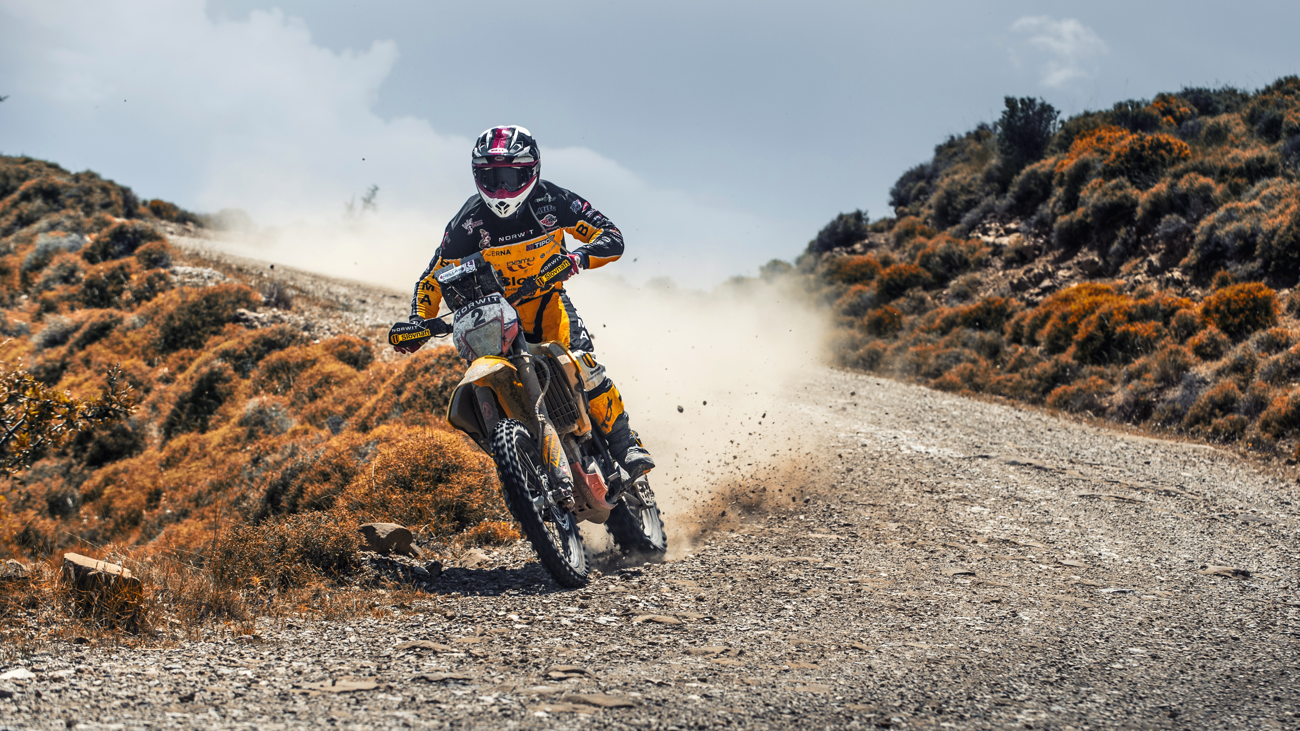 Motorcyclist racing on a dusty dirt road HD Wallpaper