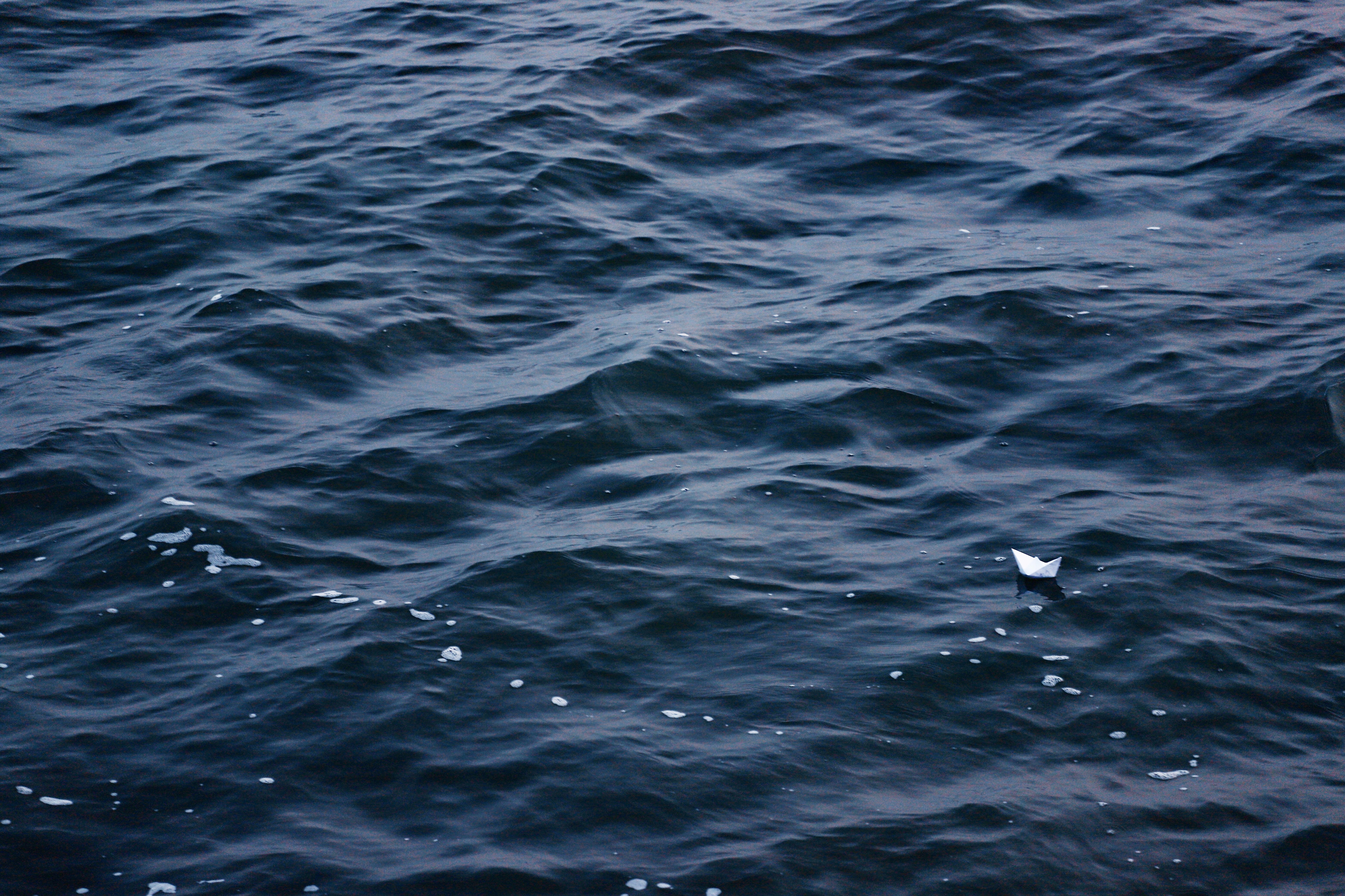 A lone paper boat floats on dark, rippling water HD Wallpaper