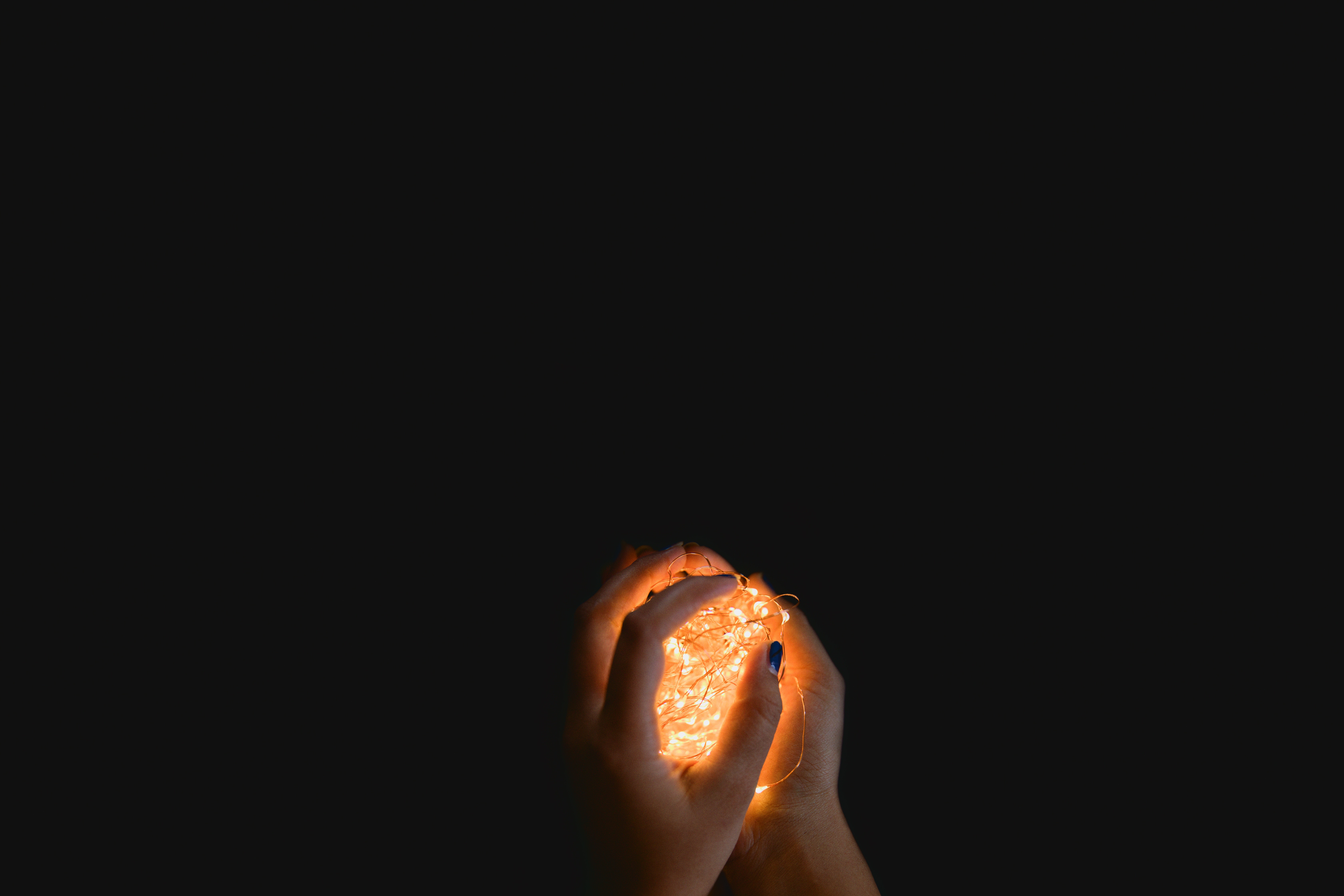 Hands holding illuminated fairy lights in darkness HD Wallpaper