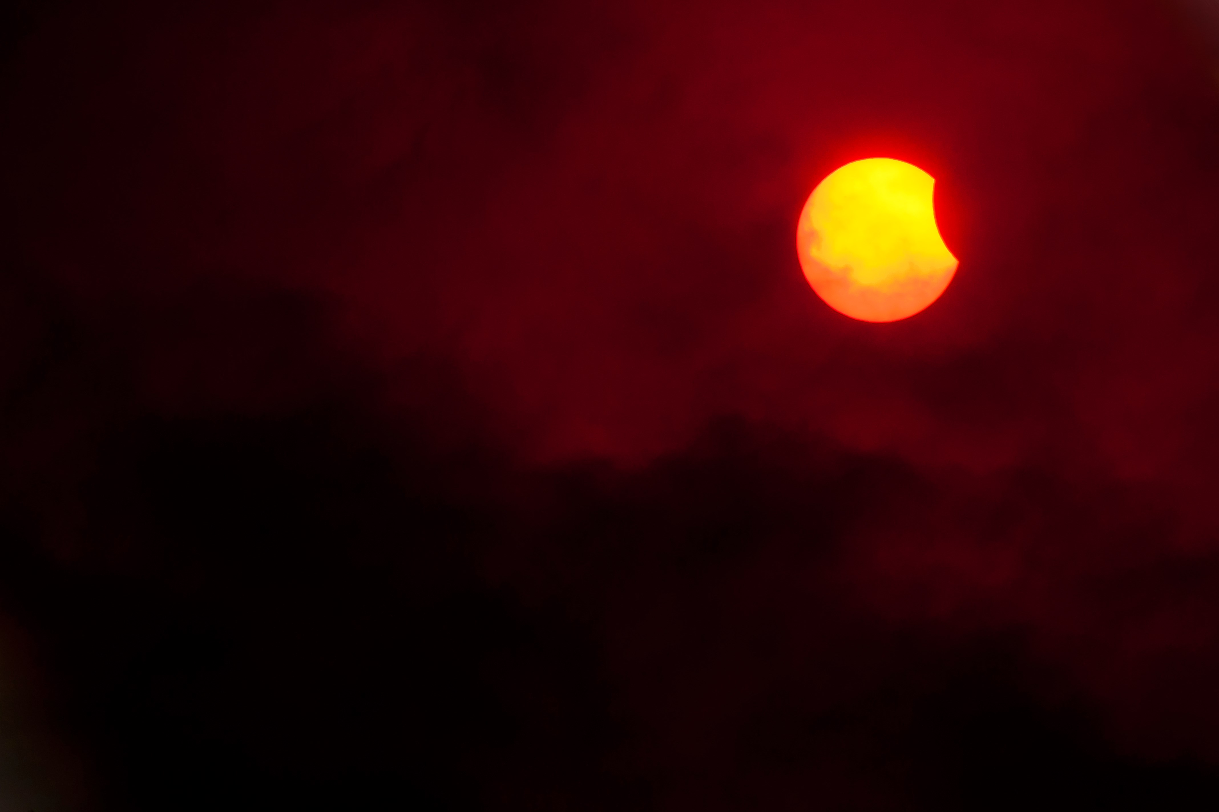 Partial solar eclipse through dark clouds HD Wallpaper