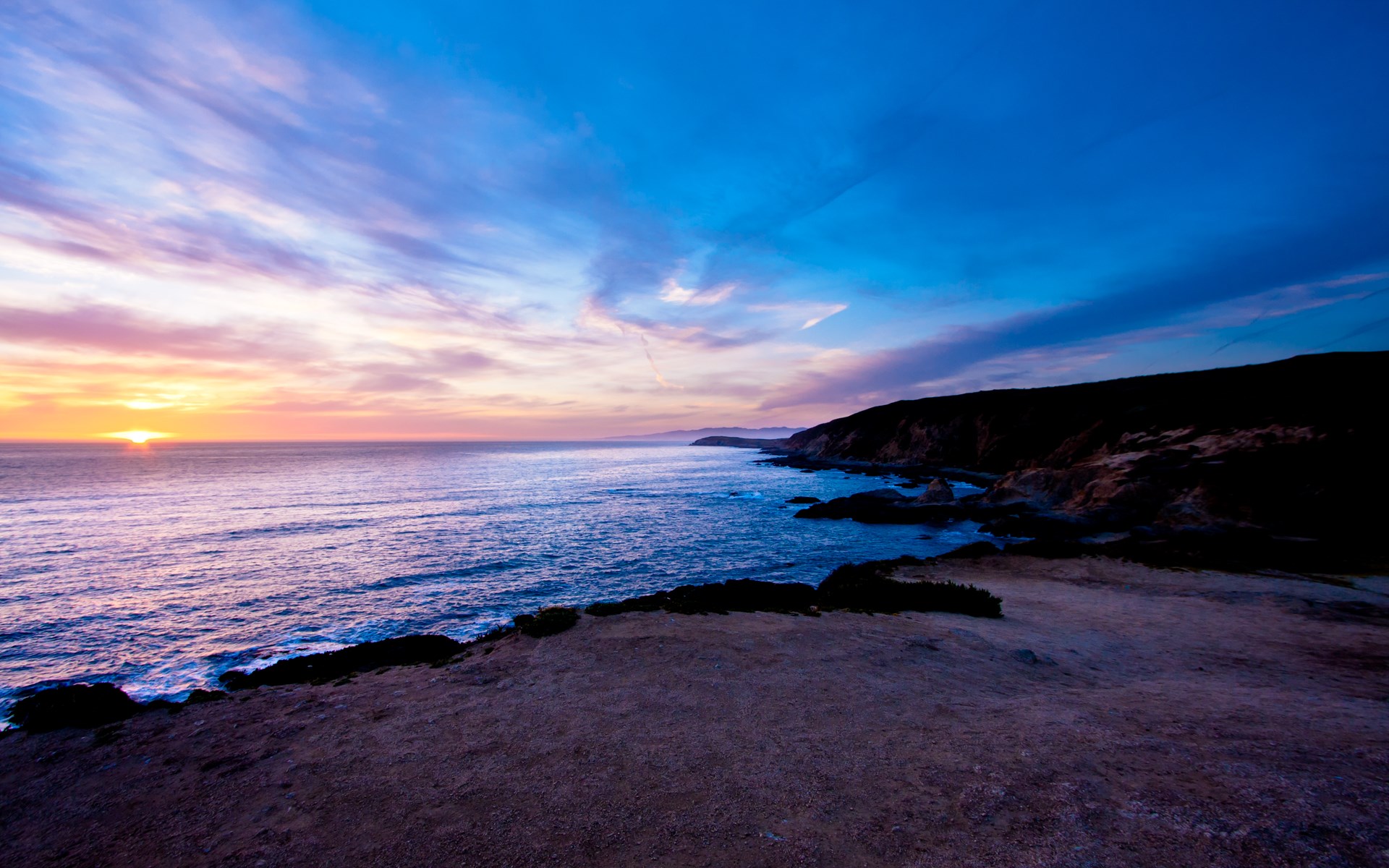 Sunset over the ocean with rocky coastline HD Wallpaper