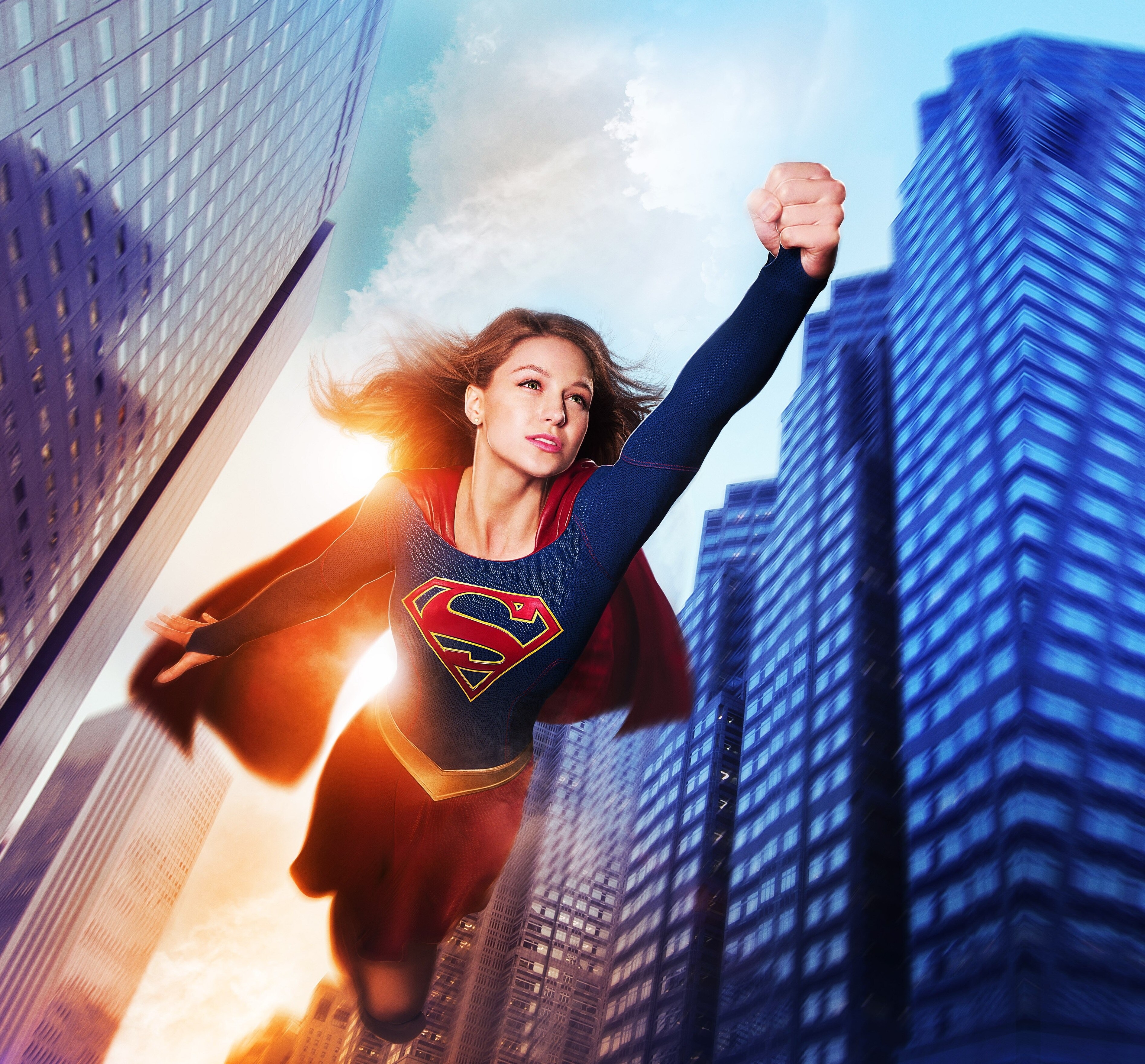 Supergirl flying through a city HD Wallpaper