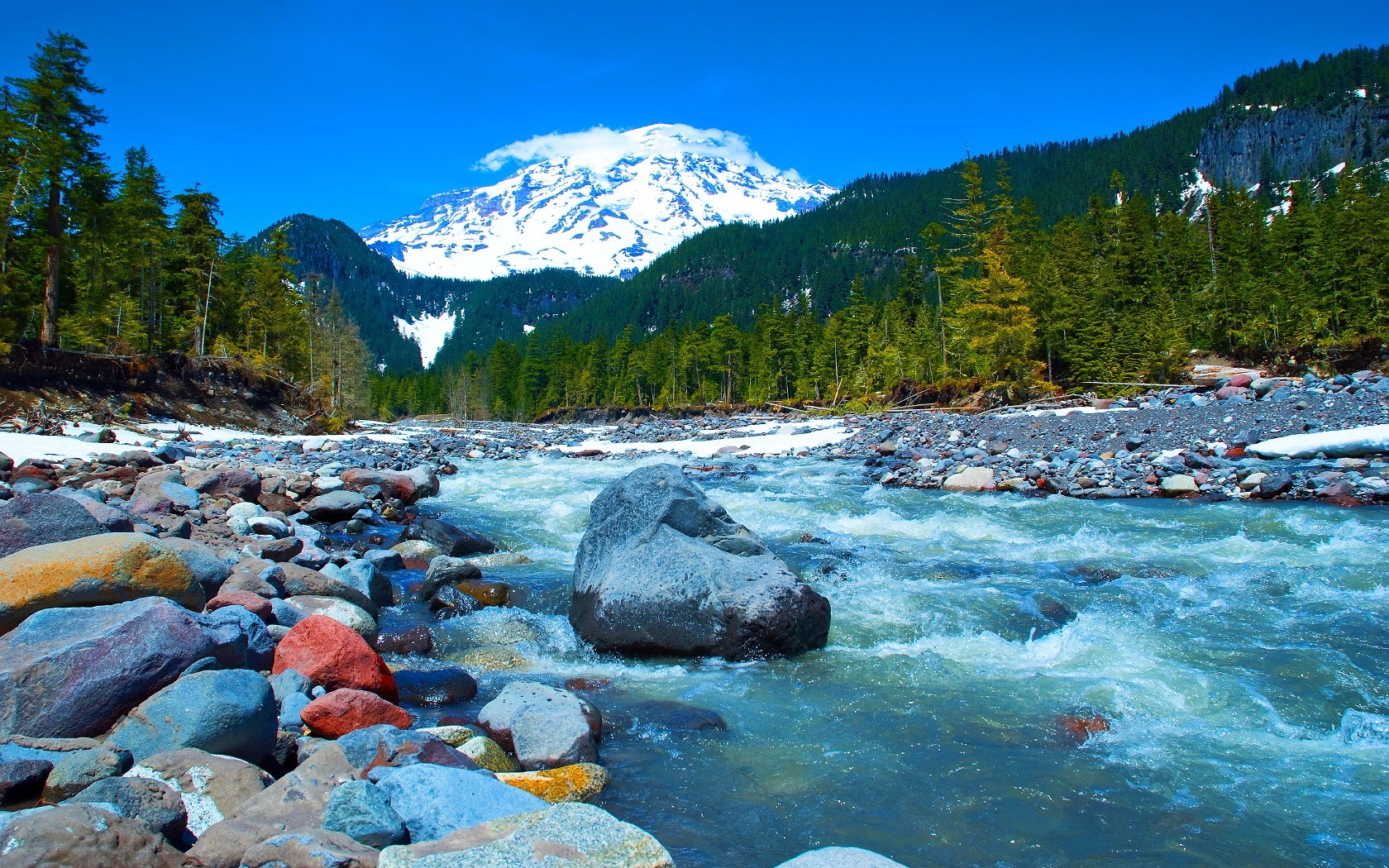 River flowing past rocks with snow-capped mountain and forest HD Wallpaper