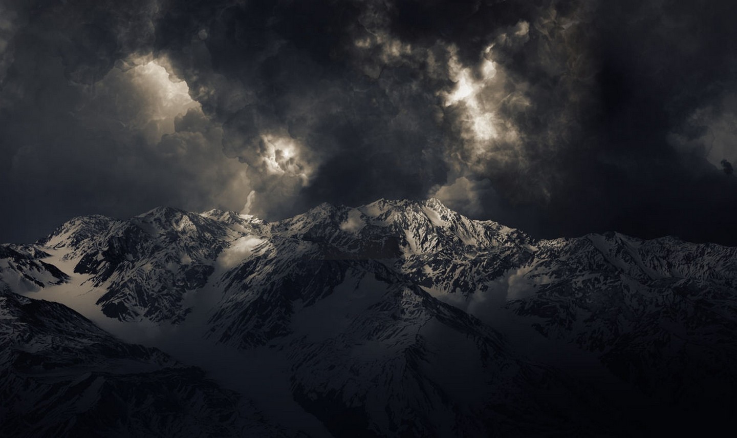 Snowy mountains under dark storm clouds with sunlight breaking through HD Wallpaper