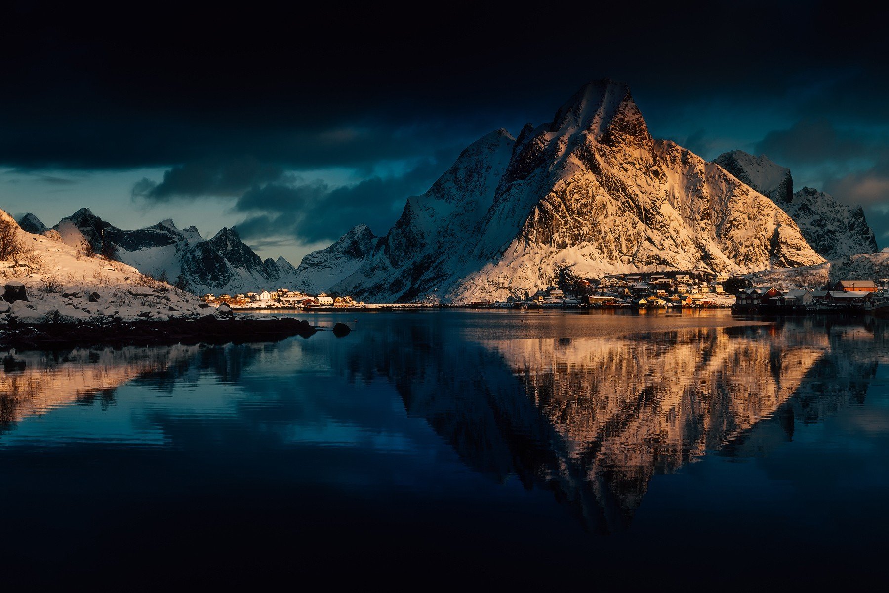 Snowy mountains and village reflected in water in Lofoten, Norway HD Wallpaper