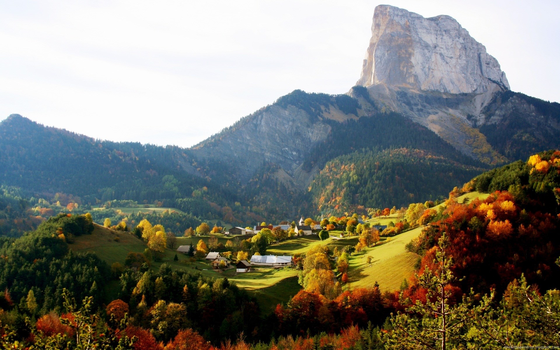 Mountain village in autumn with colorful trees and a large peak HD Wallpaper