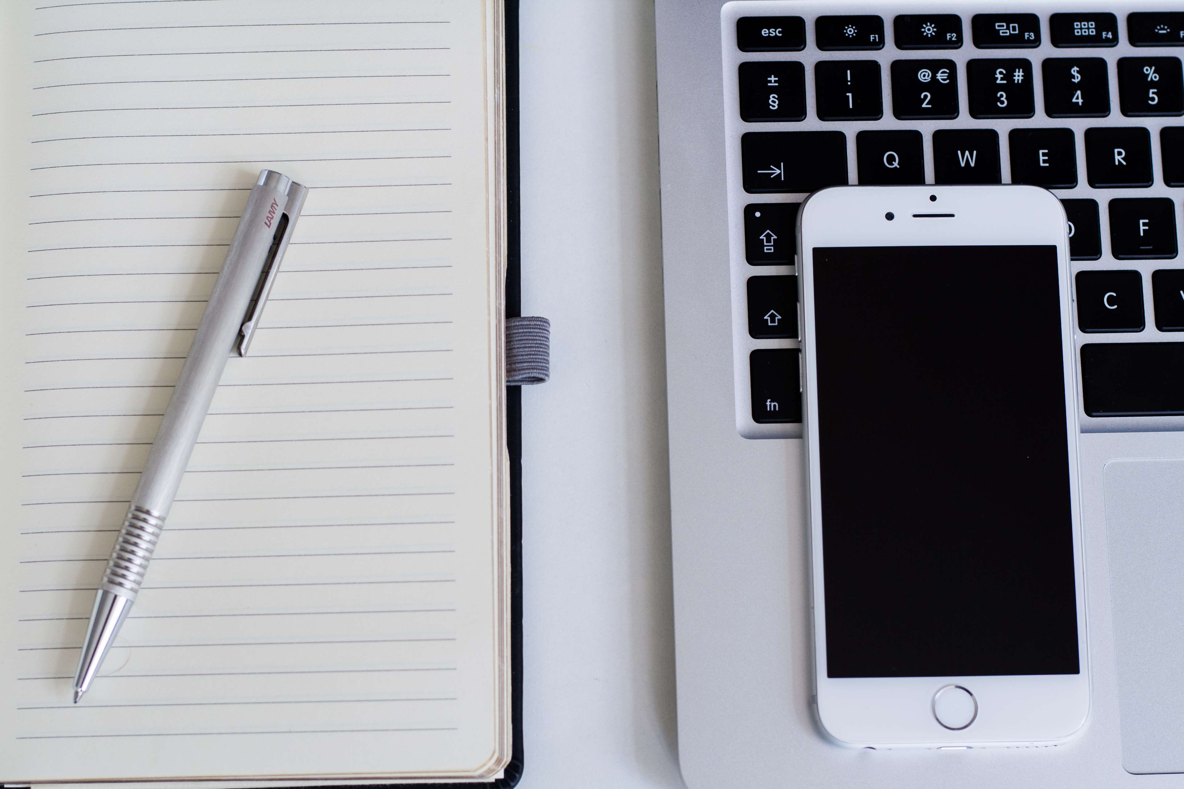 Apple laptop with iPhone, notebook, and pen HD Wallpaper
