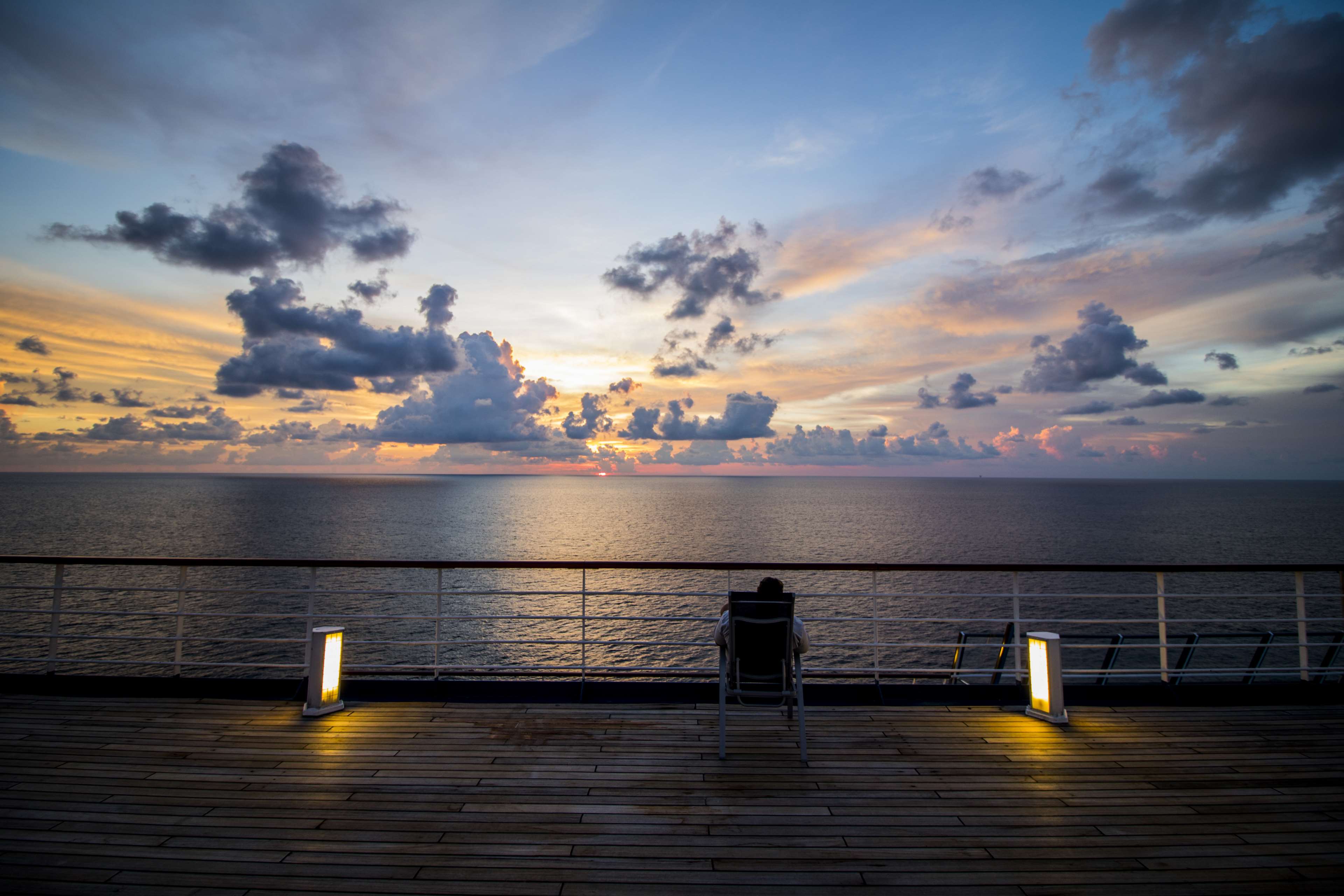 Person relaxing on a cruise ship deck at sunset HD Wallpaper