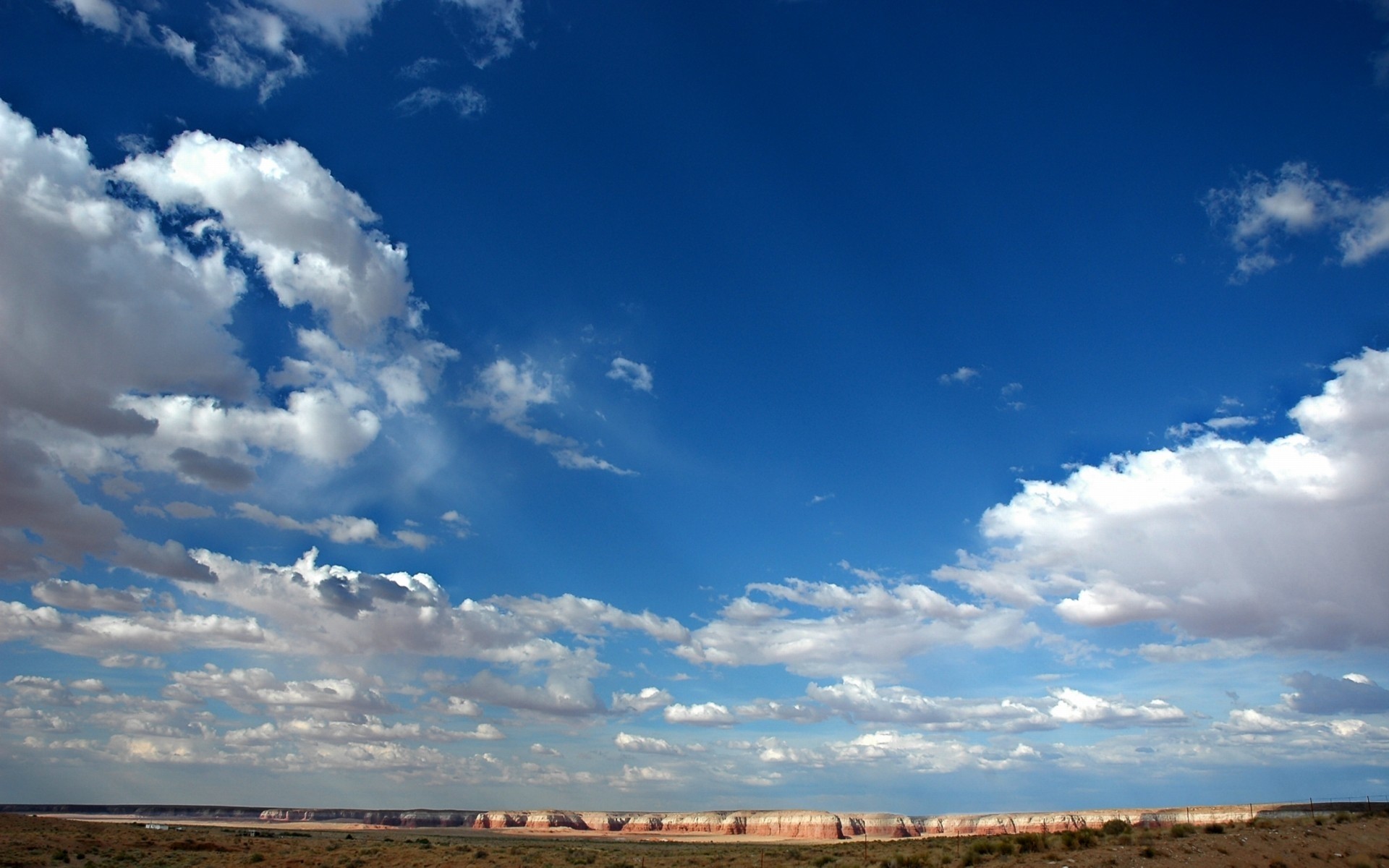 Vast blue sky with scattered clouds over a desert landscape HD Wallpaper