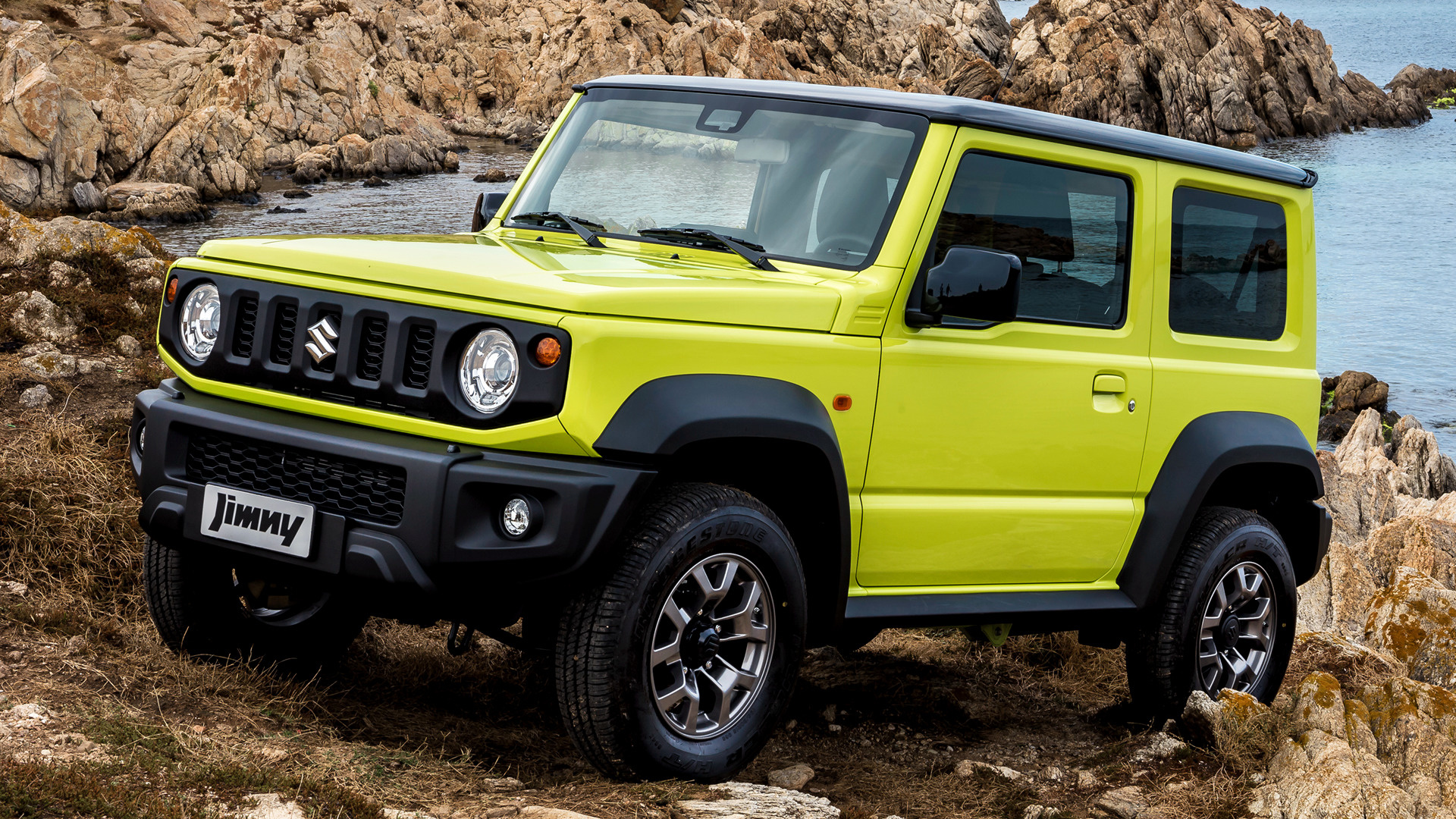 Yellow Suzuki Jimny parked on rocky terrain near water HD Wallpaper