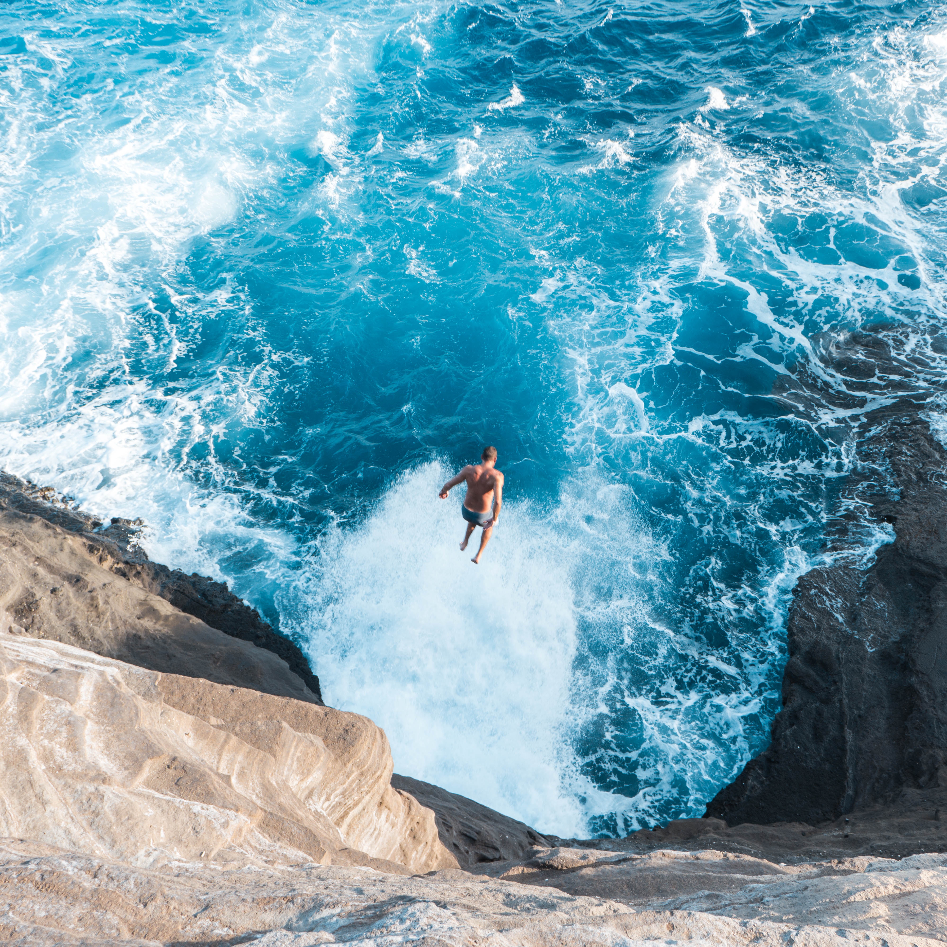 Man jumping off rocky cliff into ocean waves HD Wallpaper