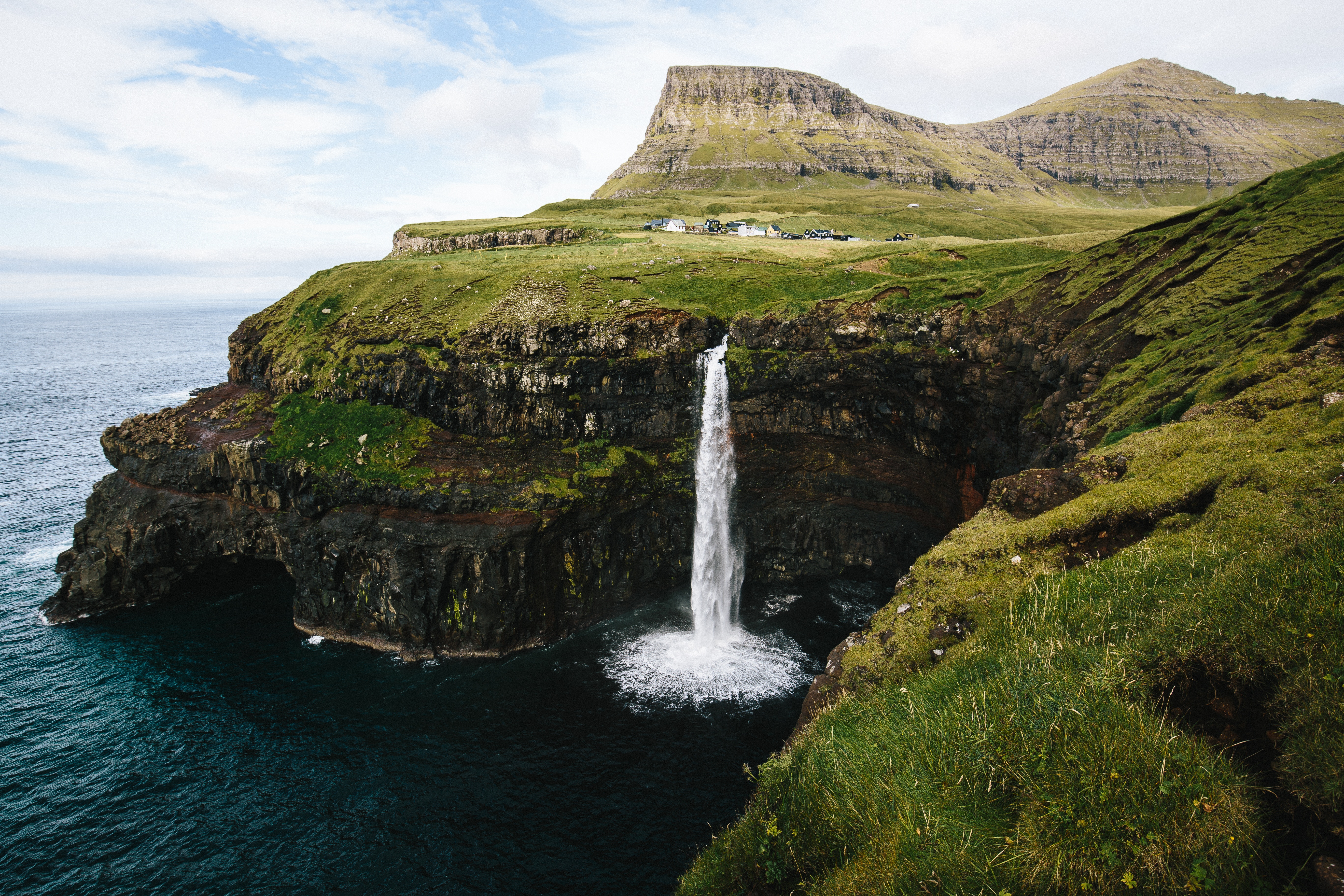 Waterfall cascading off a cliff into the ocean on Faroe Islands HD Wallpaper