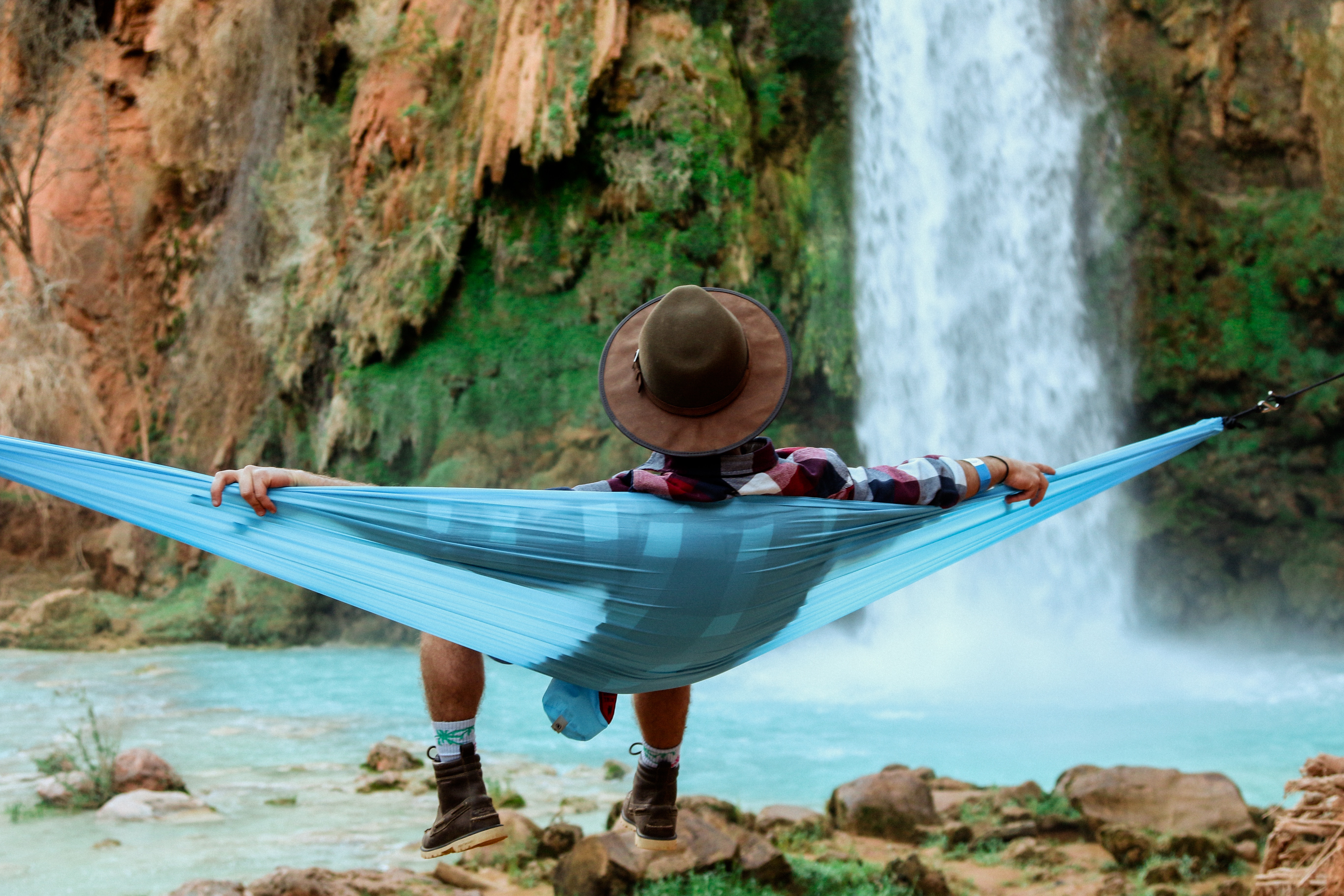 Man relaxing in a hammock near a waterfall HD Wallpaper