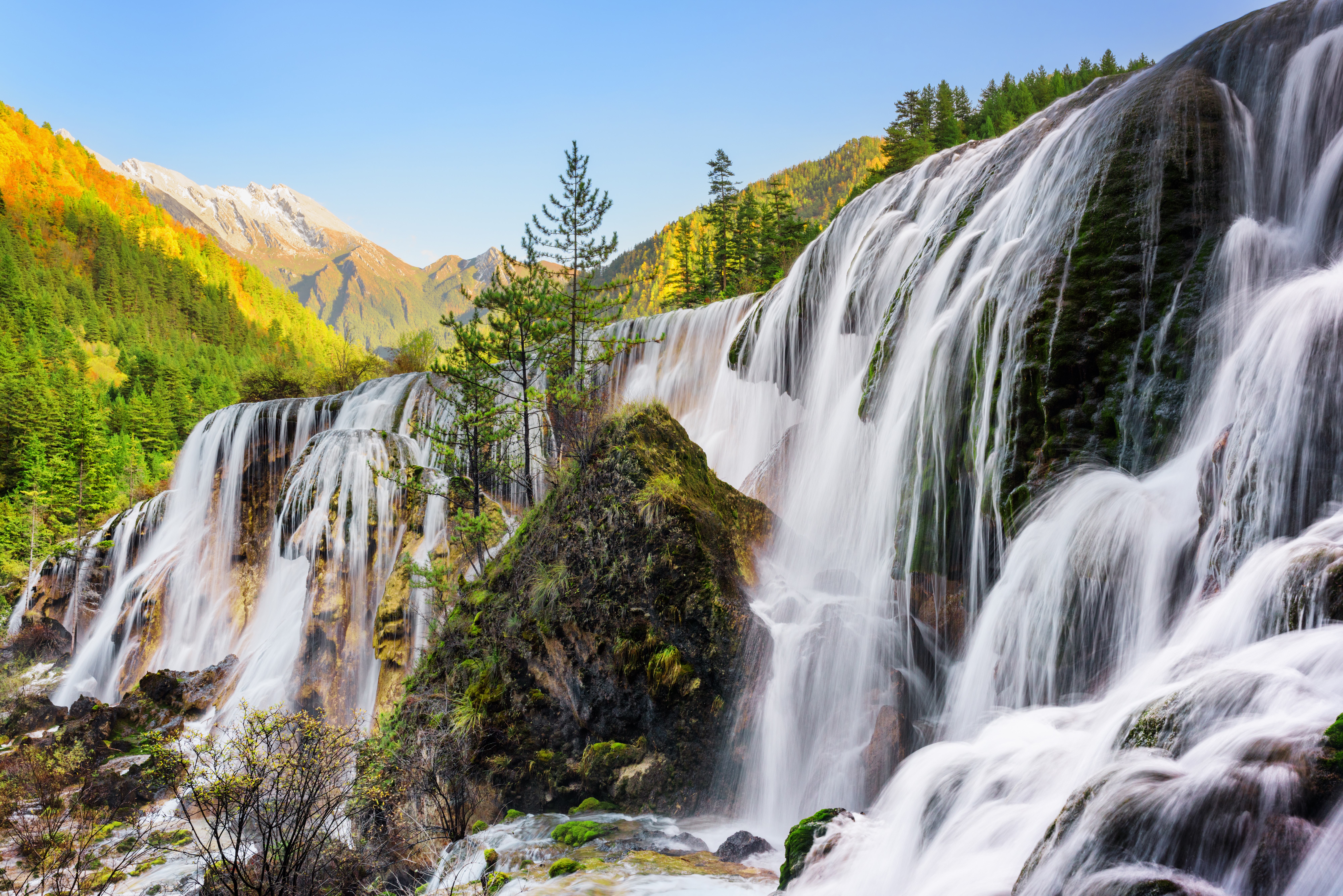 Waterfall cascading down mossy rocks with mountains and forest HD Wallpaper