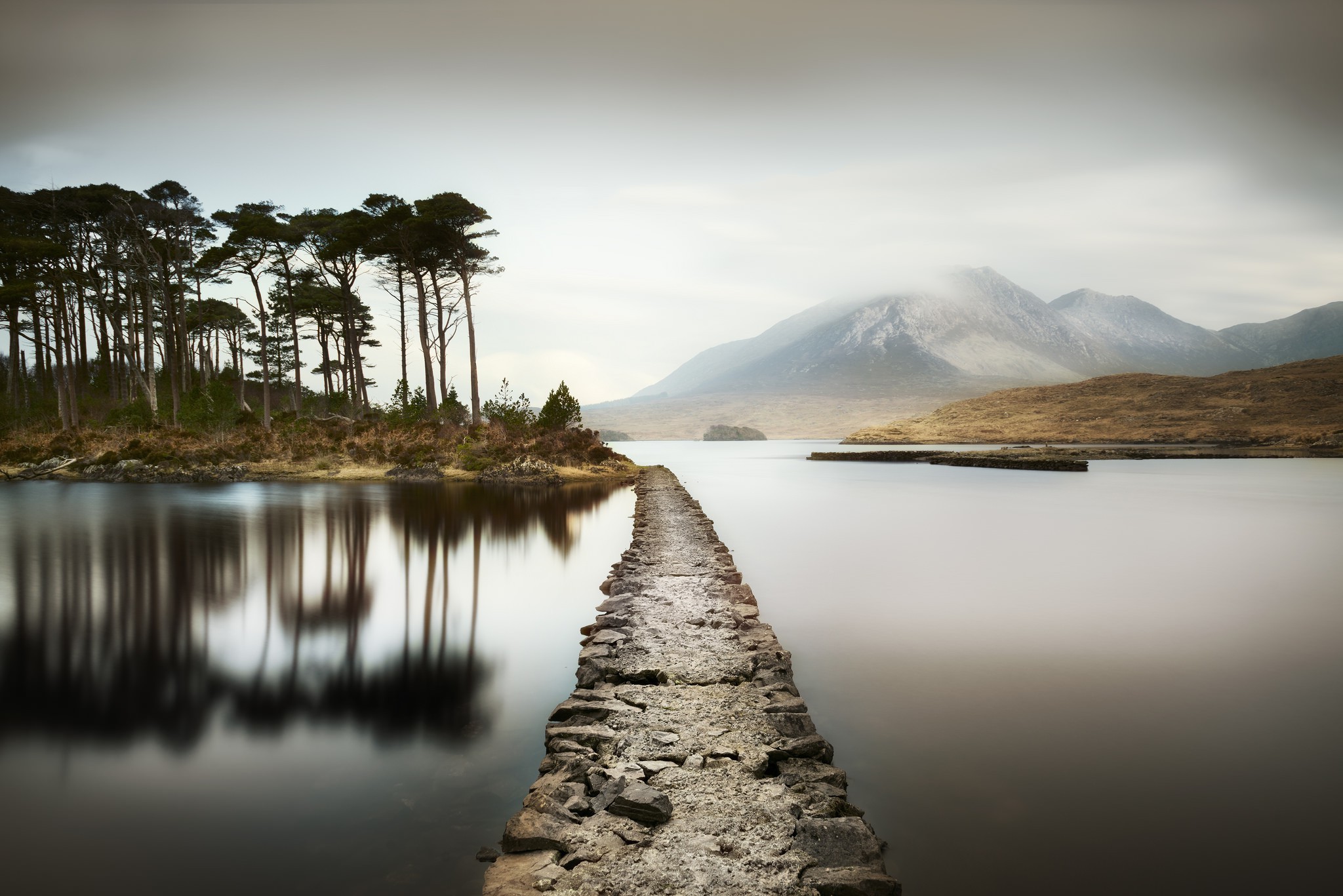 Stone path across a lake with trees and mountains HD Wallpaper