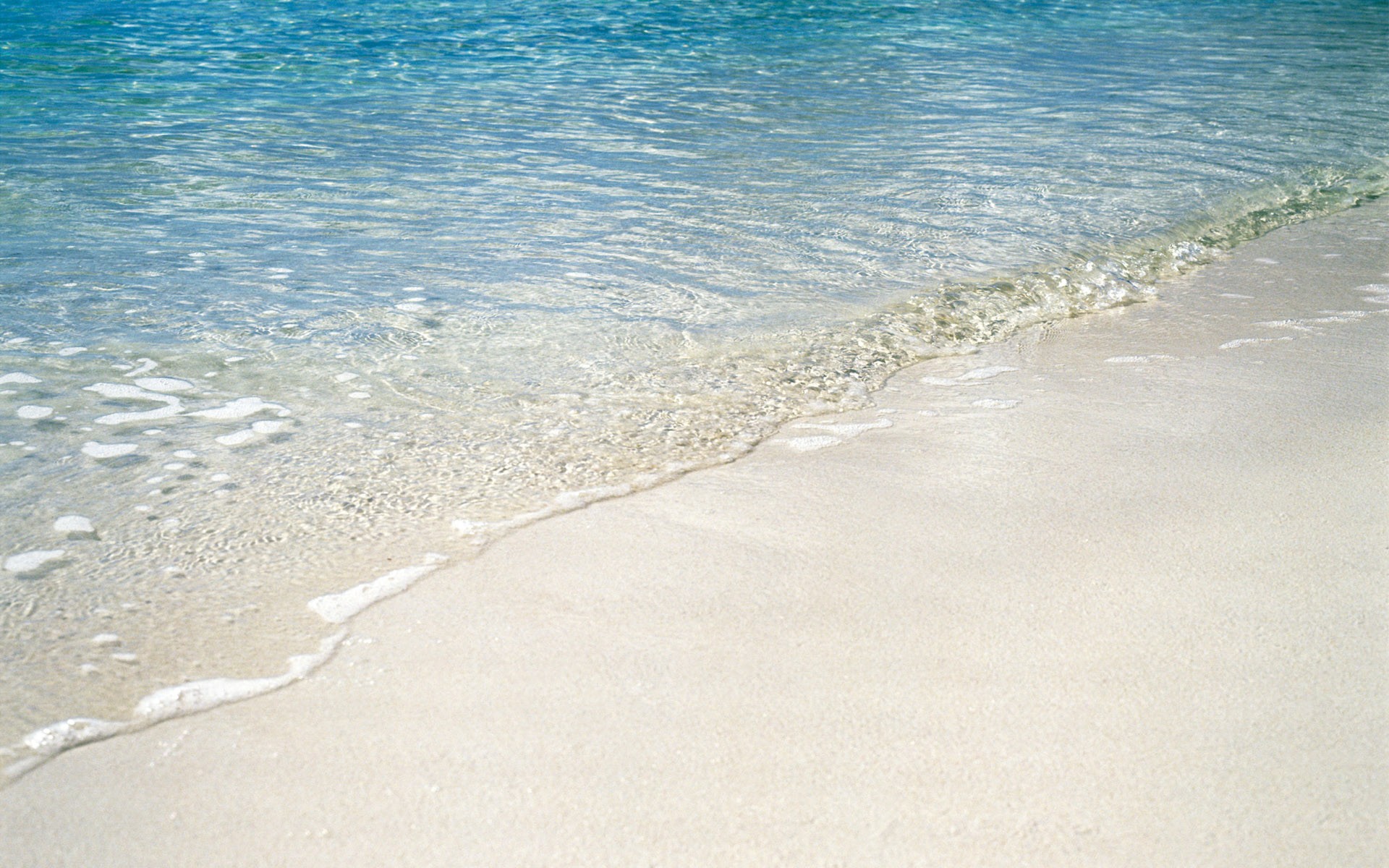 Clear ocean water washing onto a sandy beach HD Wallpaper