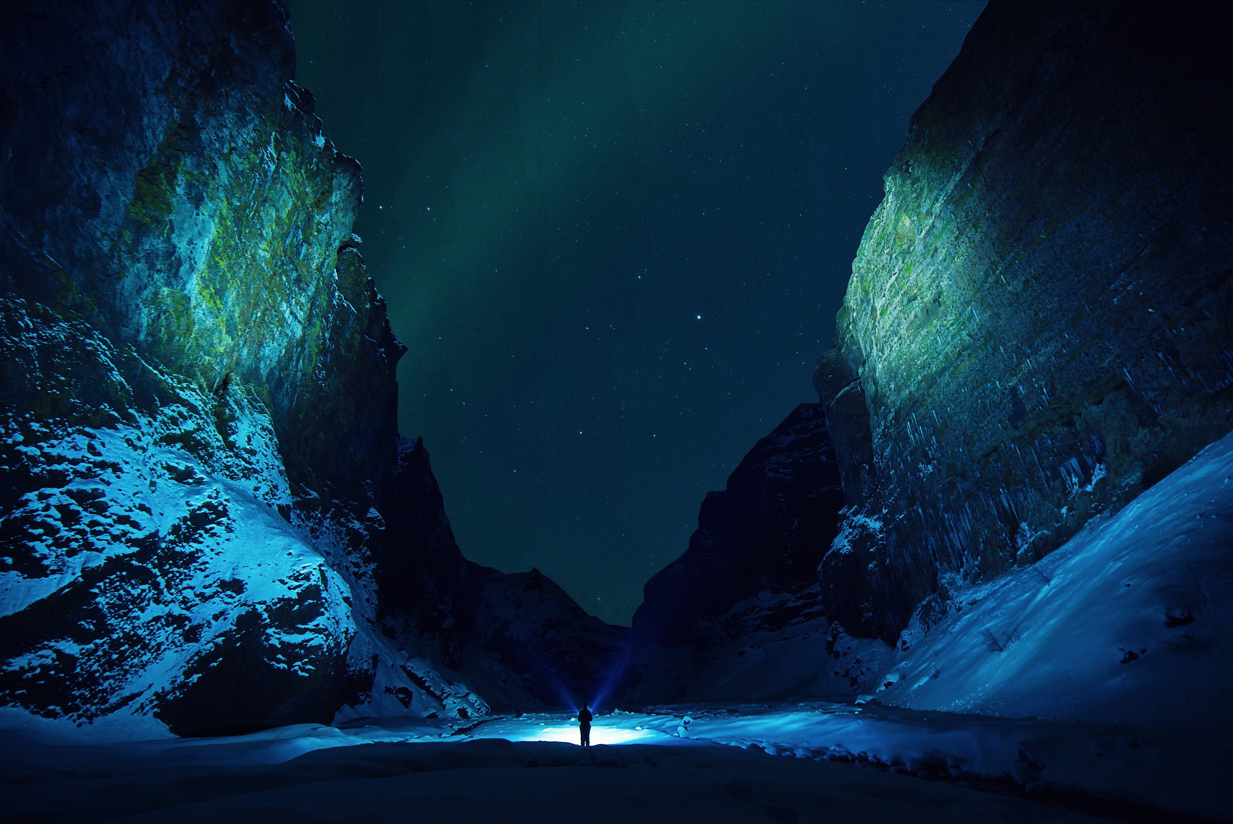 Man with flashlight in snowy canyon under aurora borealis HD Wallpaper