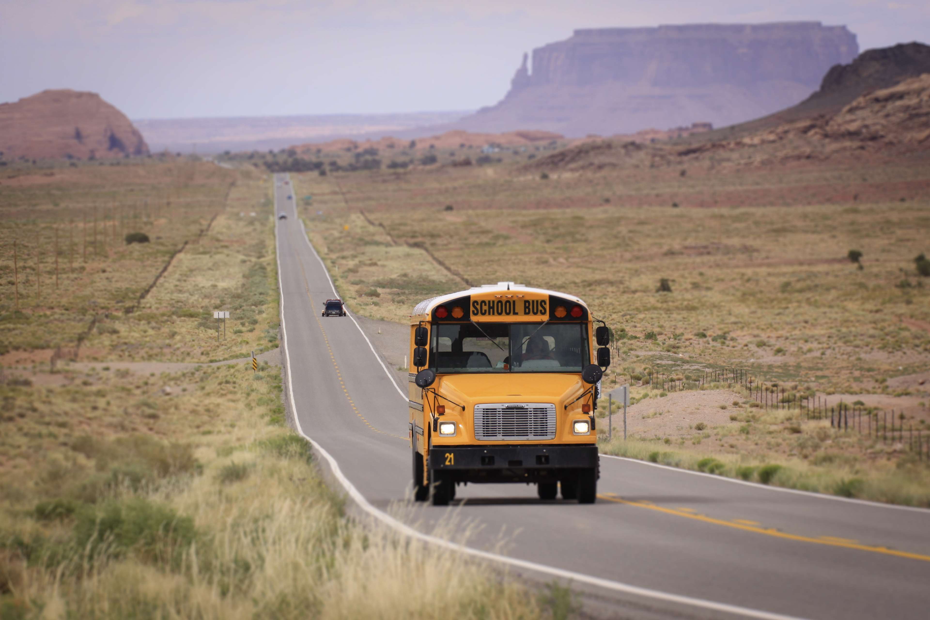 Yellow school bus driving on a desert highway in Monument Valley HD Wallpaper