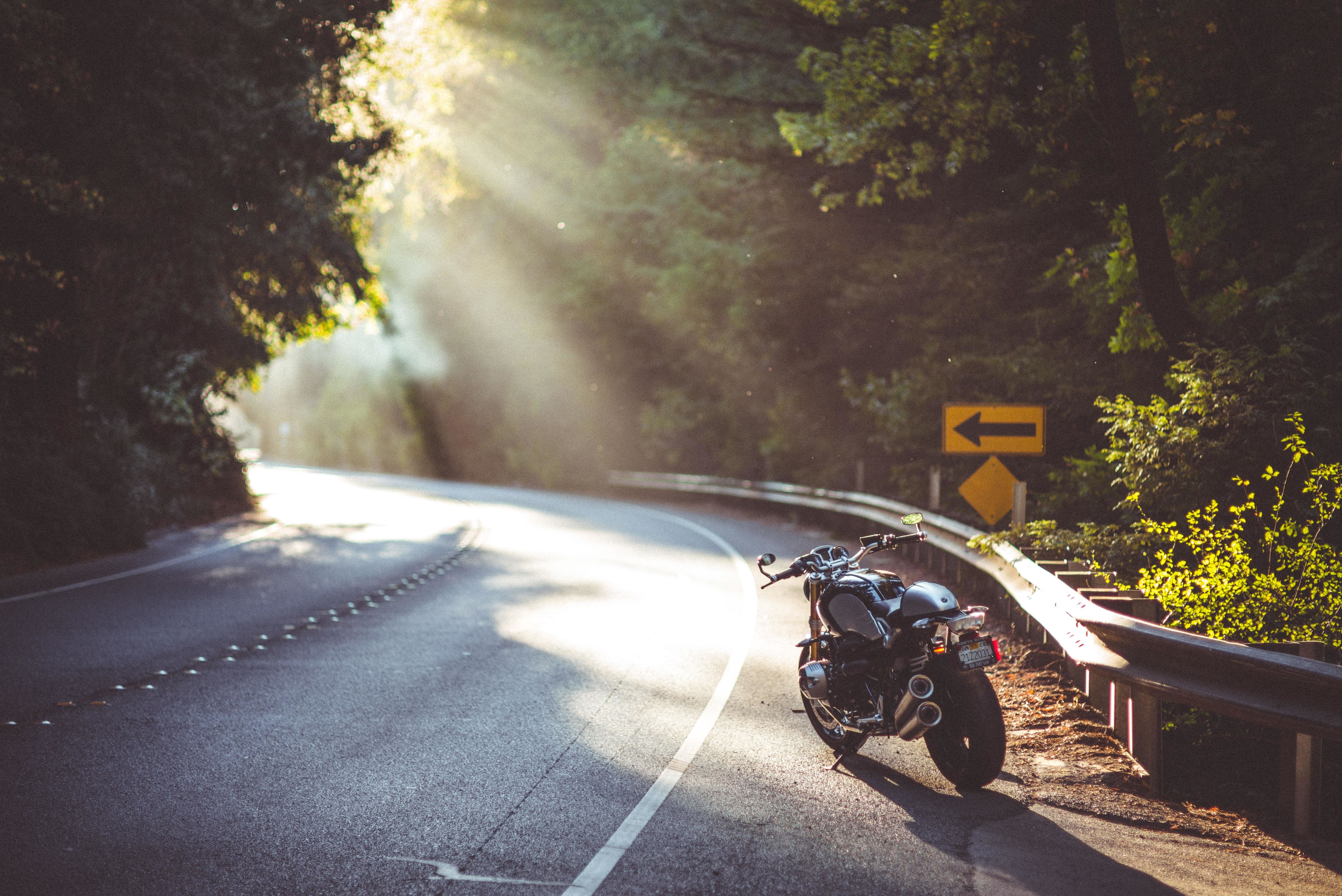 Motorcycle parked on a winding road with sunbeams HD Wallpaper
