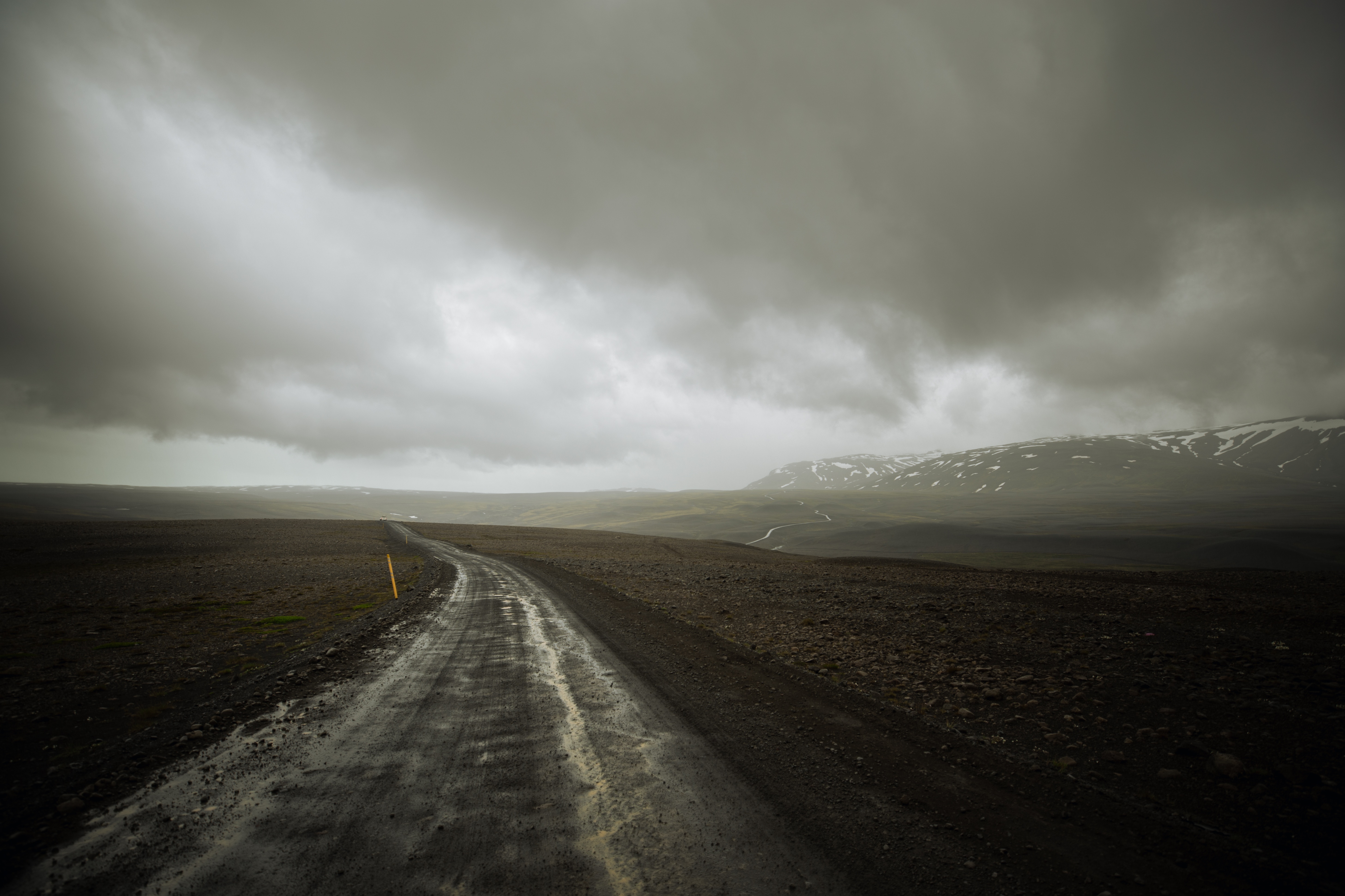 A Wet Road Through a Barren Landscape in Iceland Under Stormy Skies HD Wallpaper