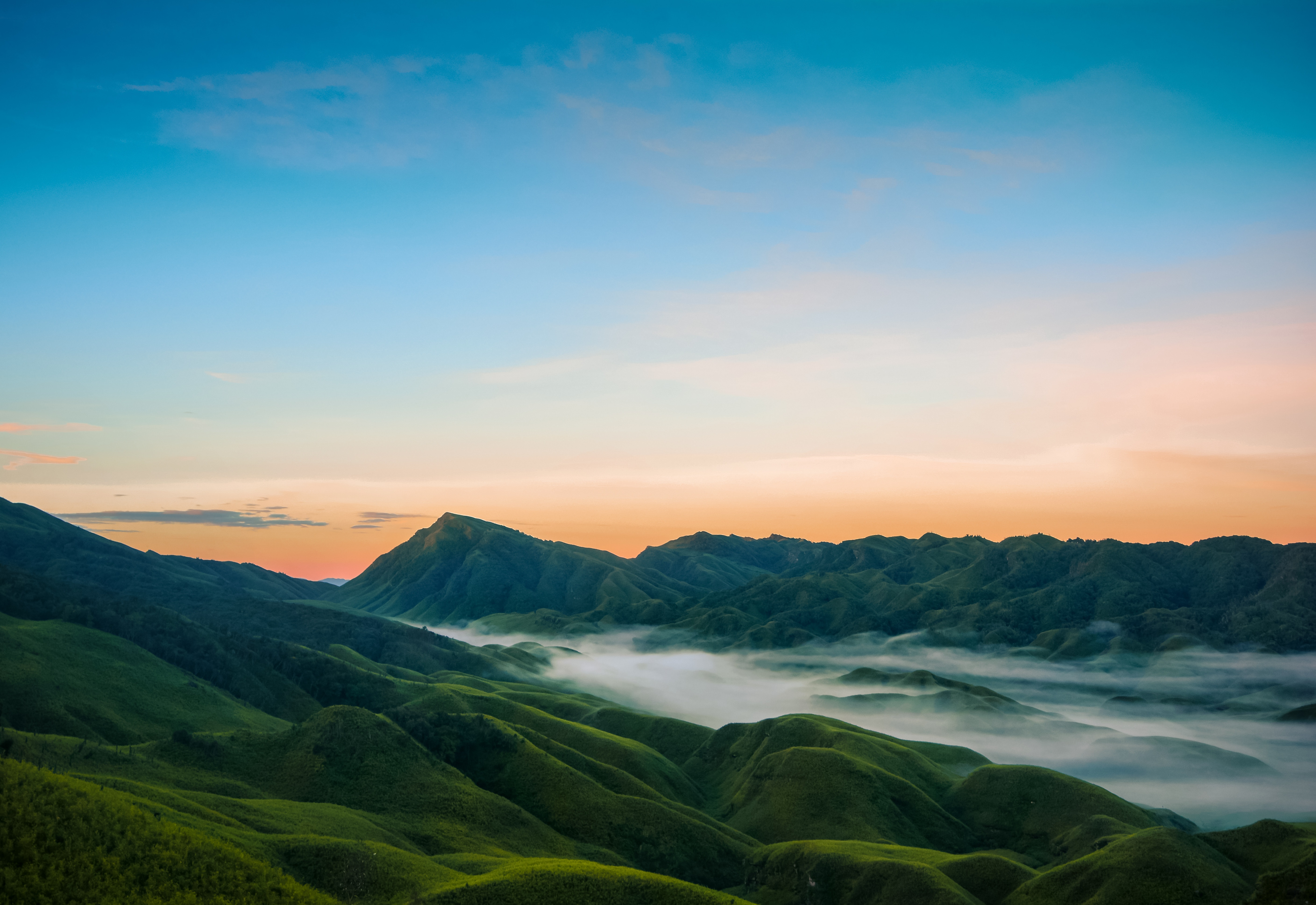 Rolling green hills and mountains at sunrise with mist HD Wallpaper
