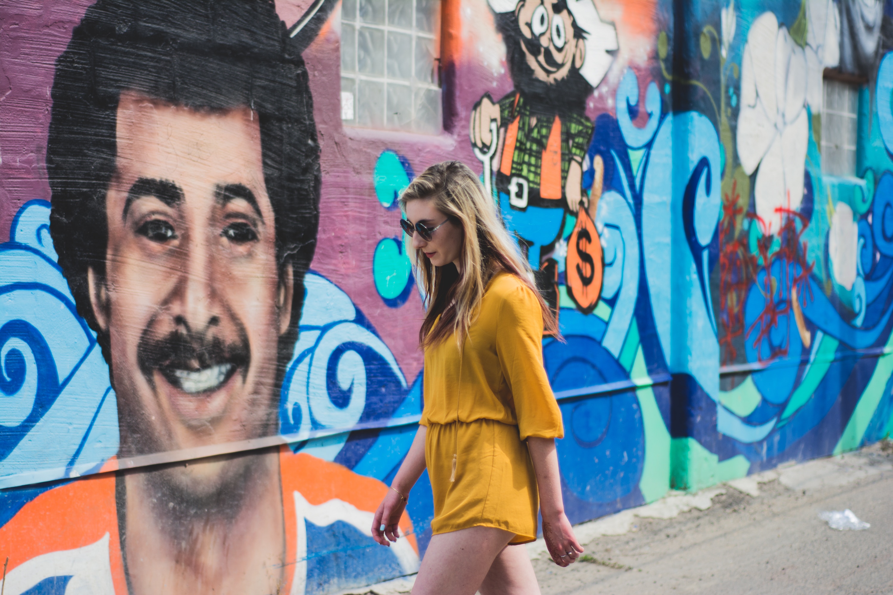 Woman walking past a mural of a man and cartoon character HD Wallpaper