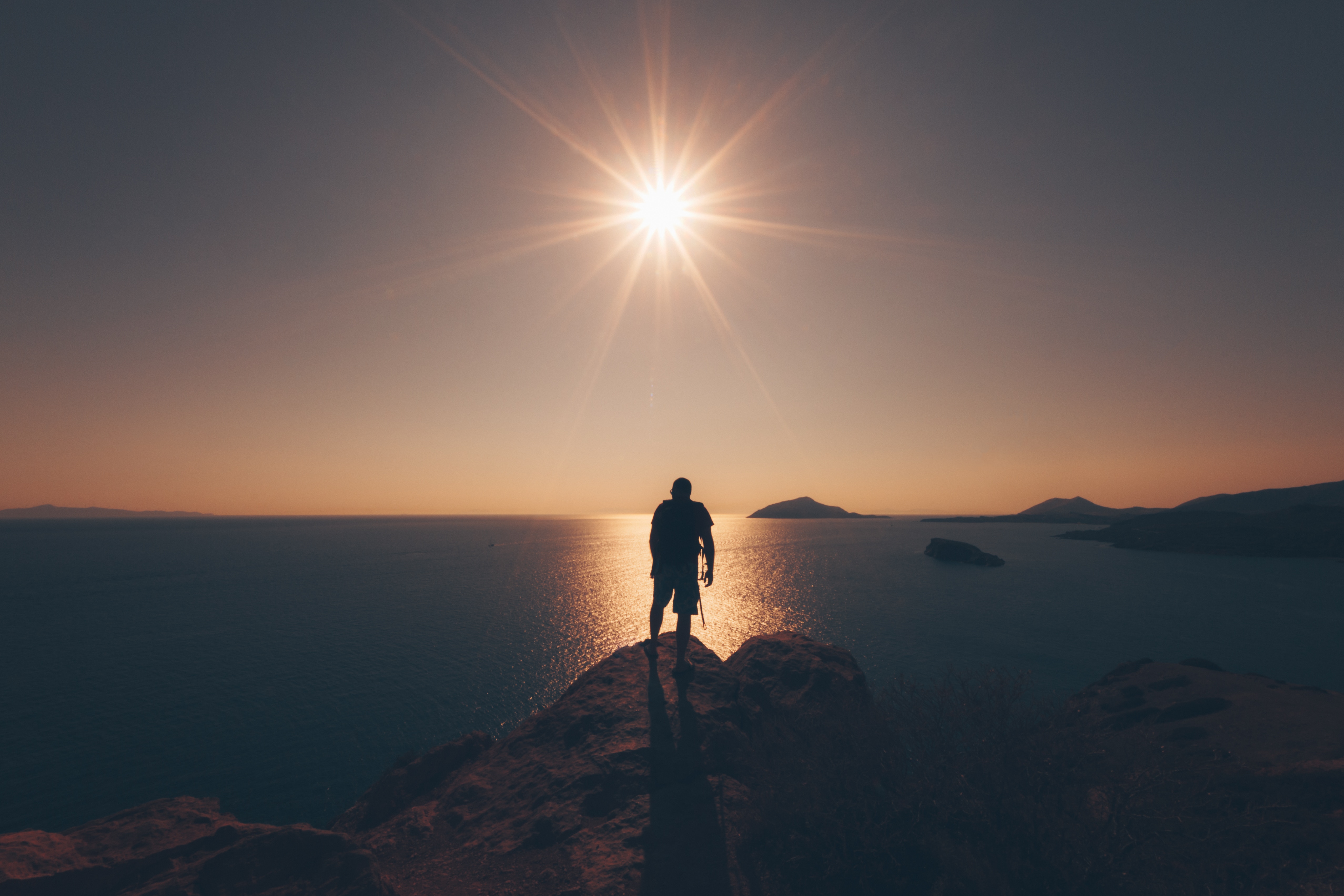 Silhouette of a person on a cliff overlooking the ocean at sunset HD Wallpaper
