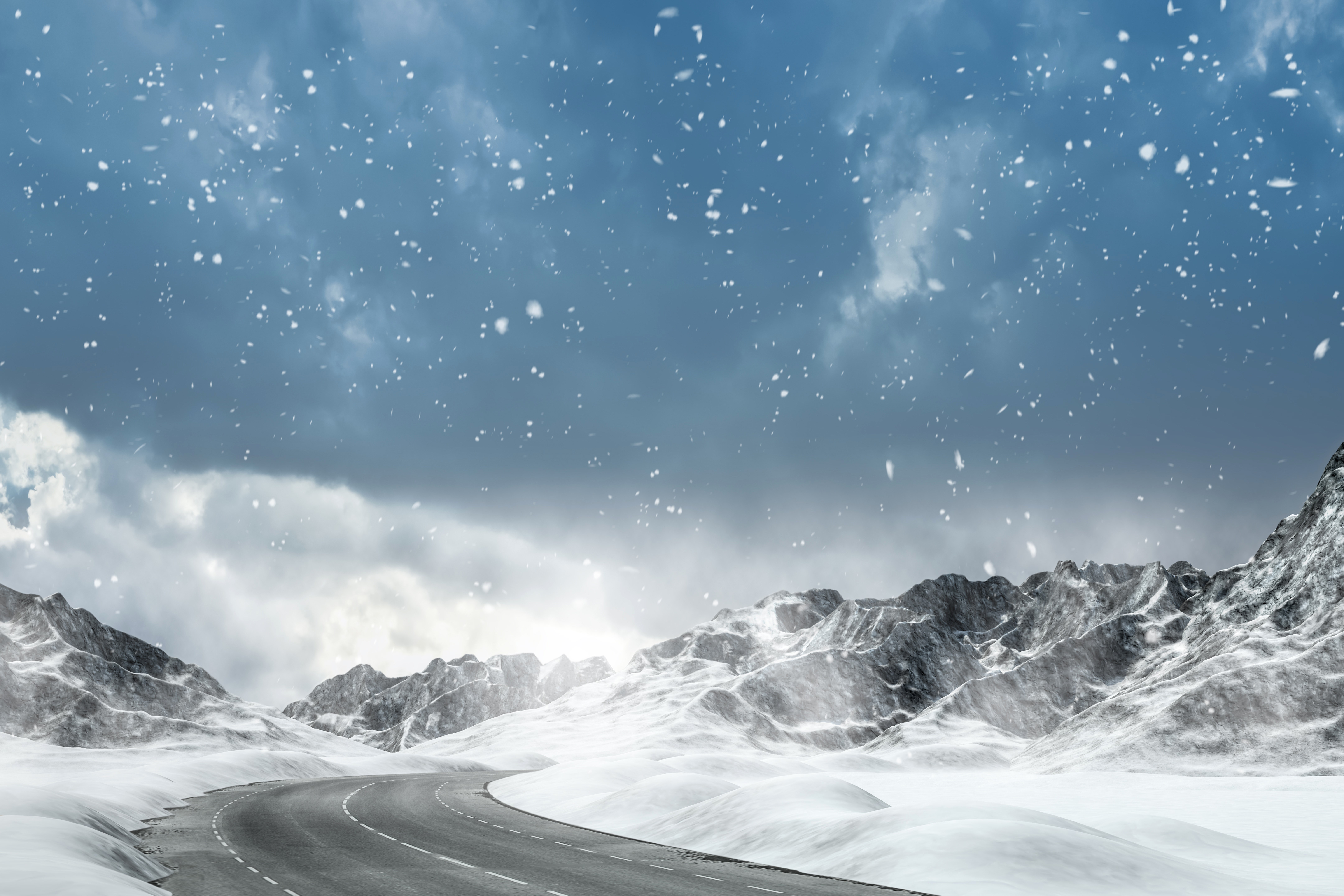 Winding road through snowy mountains with falling snow HD Wallpaper