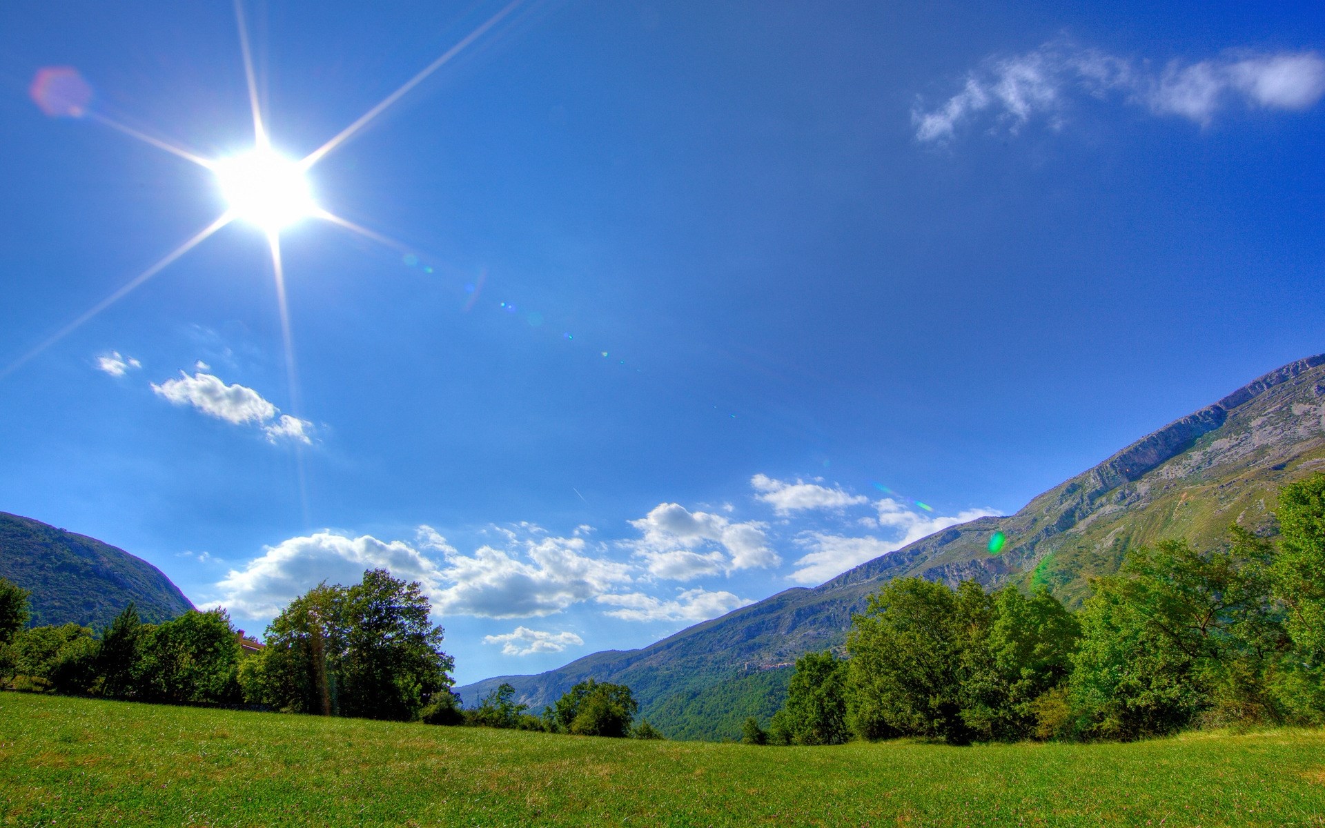 Sunny day over a green meadow and mountains HD Wallpaper