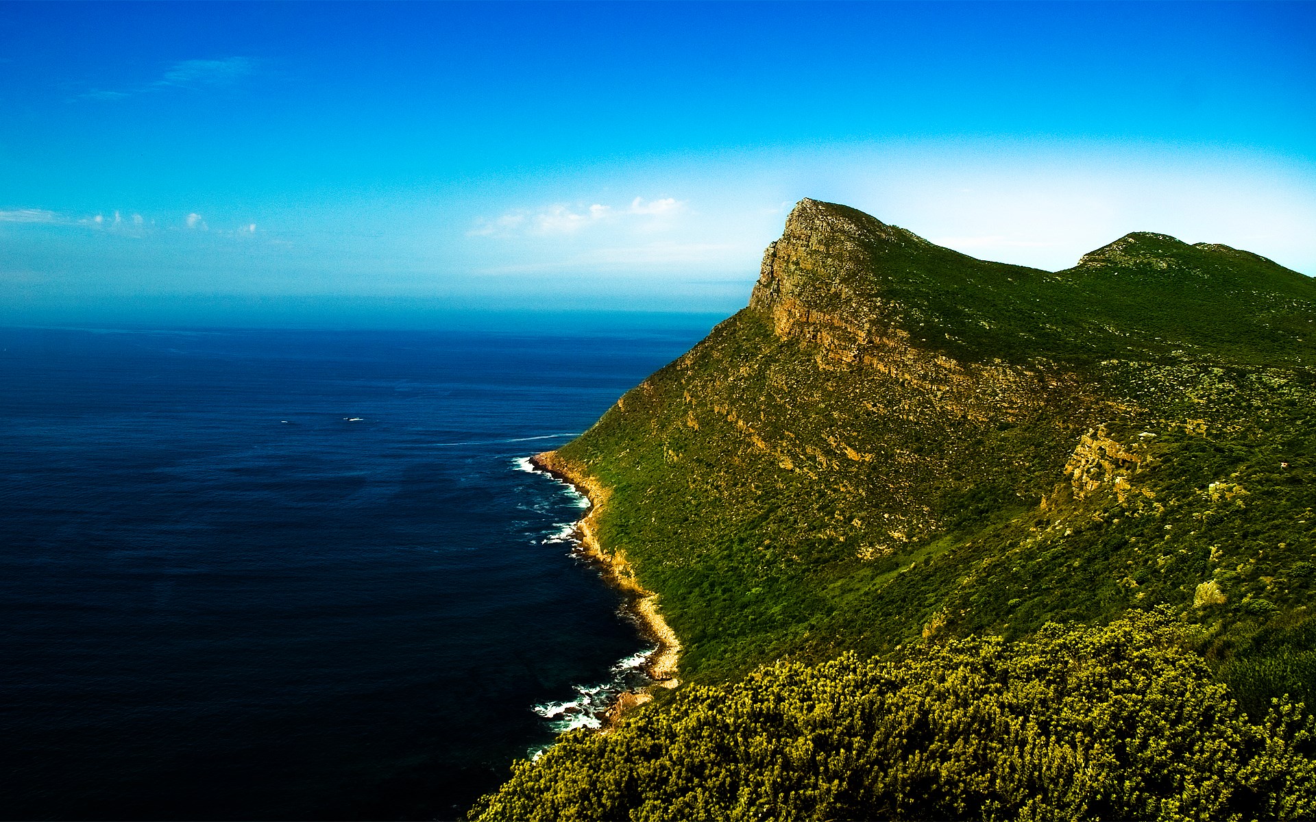 Green mountain overlooking a dark blue ocean under a clear sky HD Wallpaper