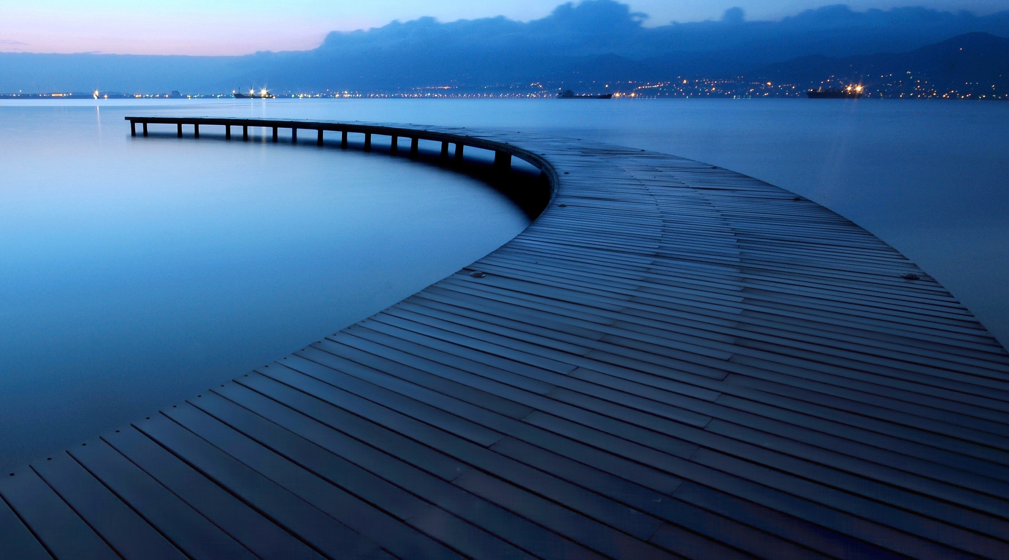 Curved wooden pier on a calm lake at dusk HD Wallpaper