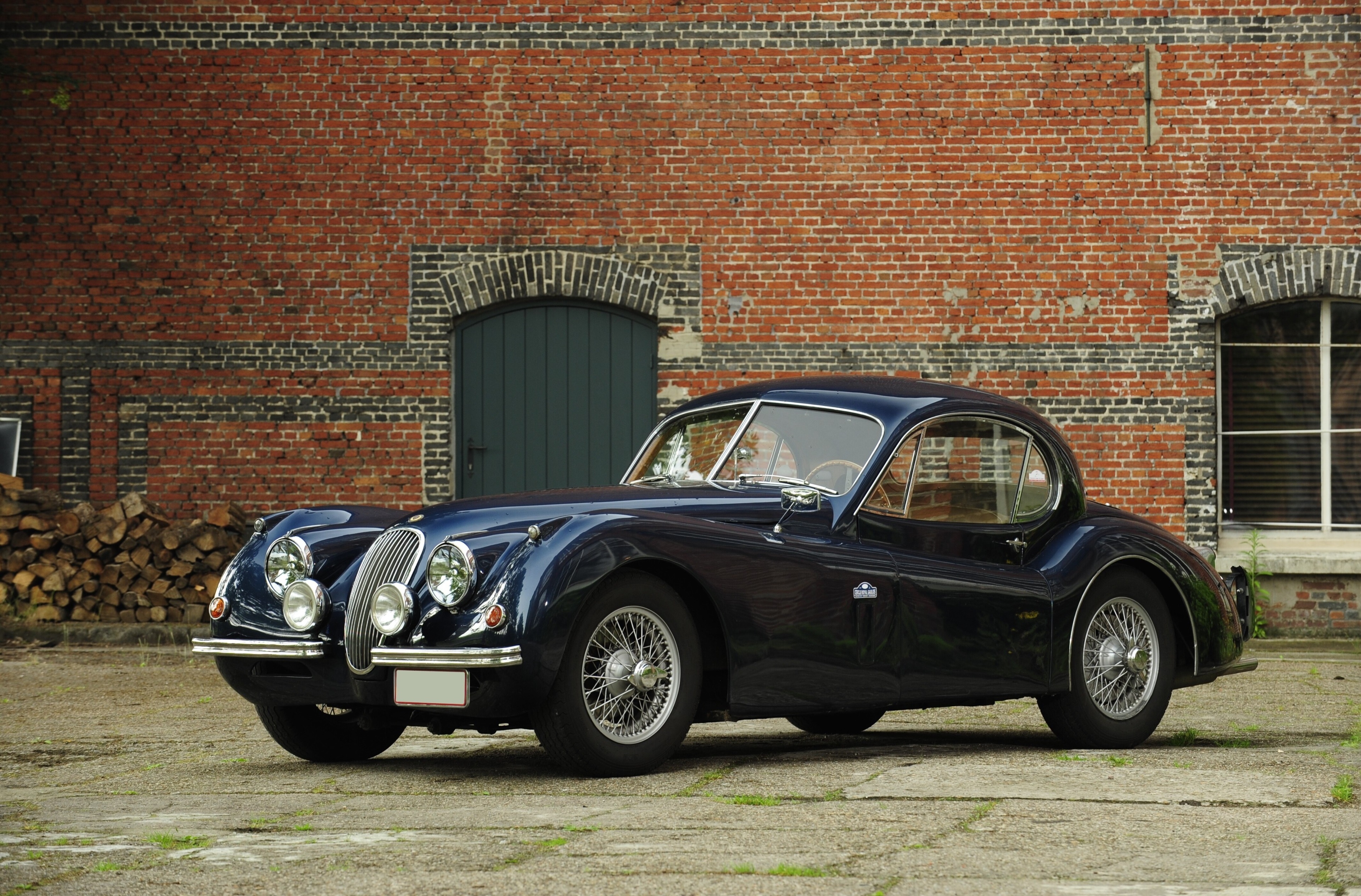 Jaguar XK120 coupe in front of a brick building HD Wallpaper