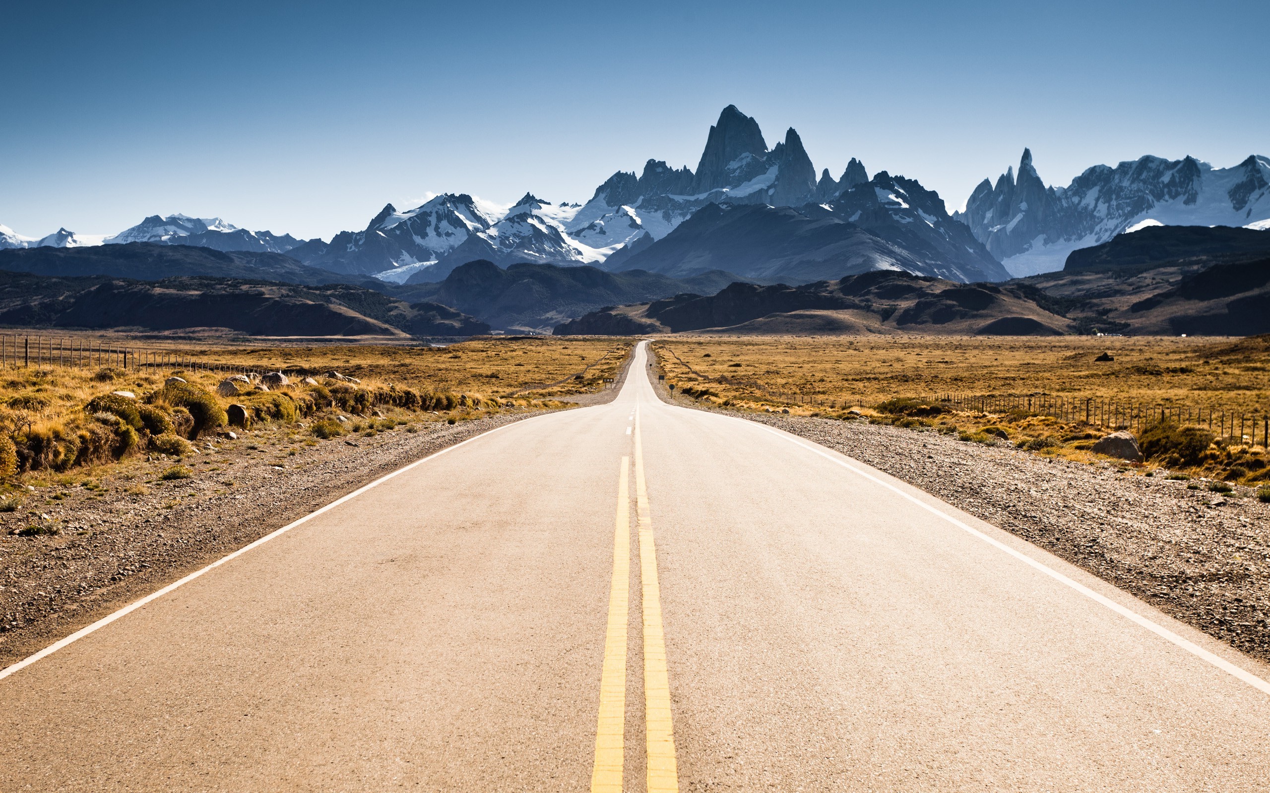 Road leading to snowy mountain peaks under clear sky HD Wallpaper