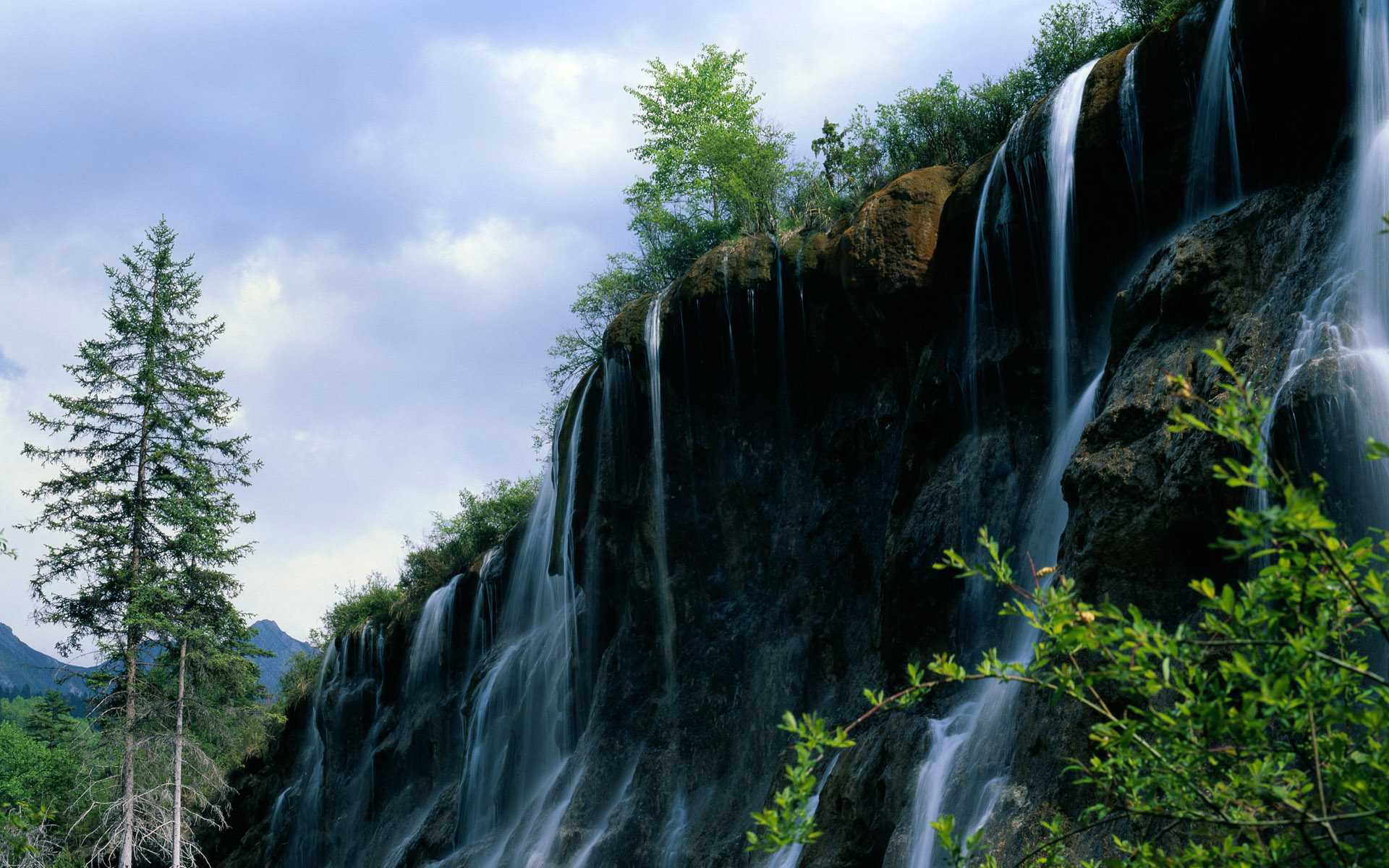 Waterfall cascading over a rocky cliff with trees HD Wallpaper