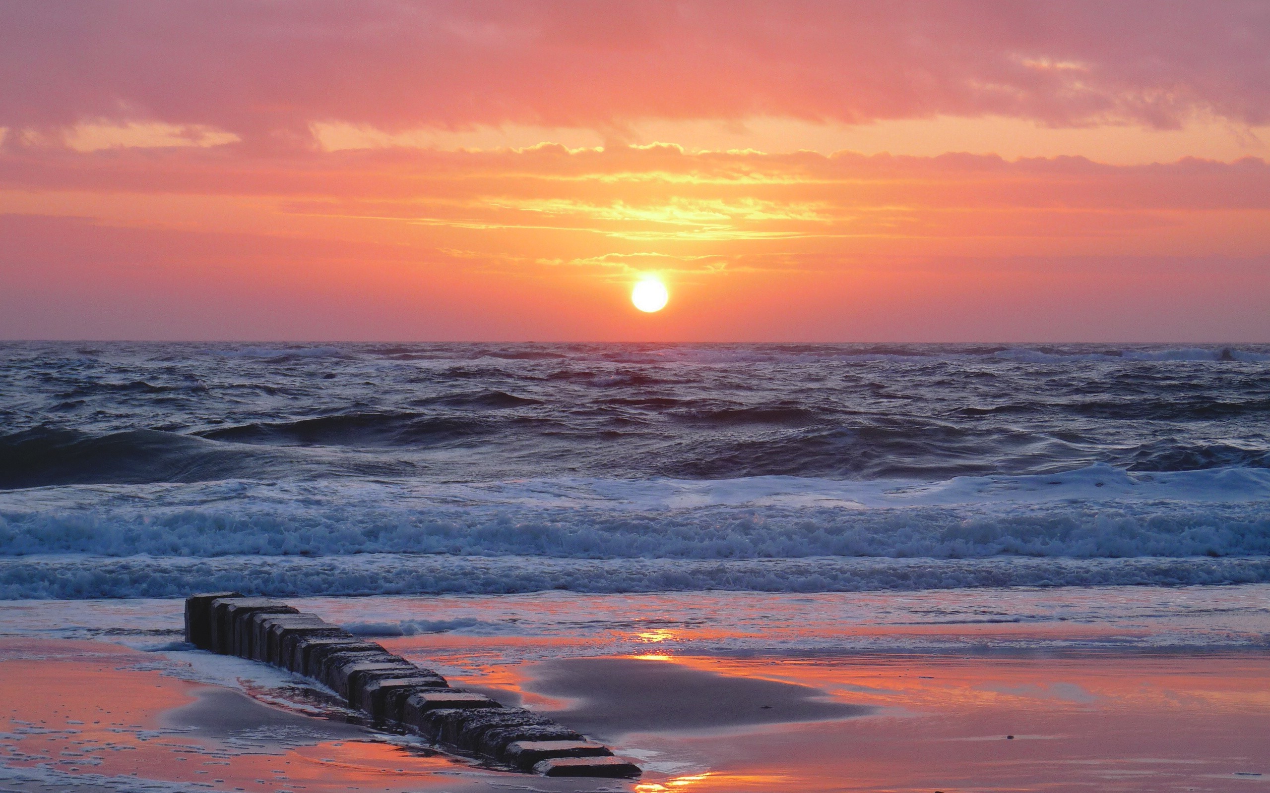 Sunset over the ocean with waves and a breakwater HD Wallpaper