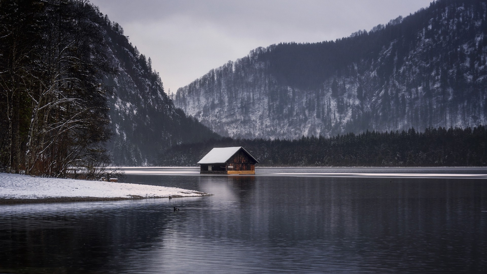 Wooden cabin on a lake with snow-covered mountains HD Wallpaper