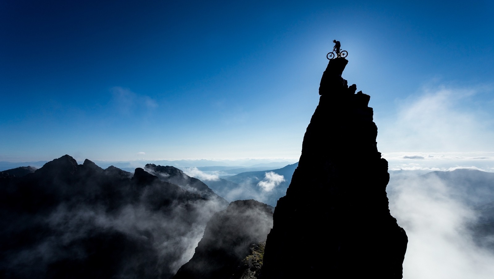 Mountain biker silhouetted on a rocky summit at sunrise HD Wallpaper