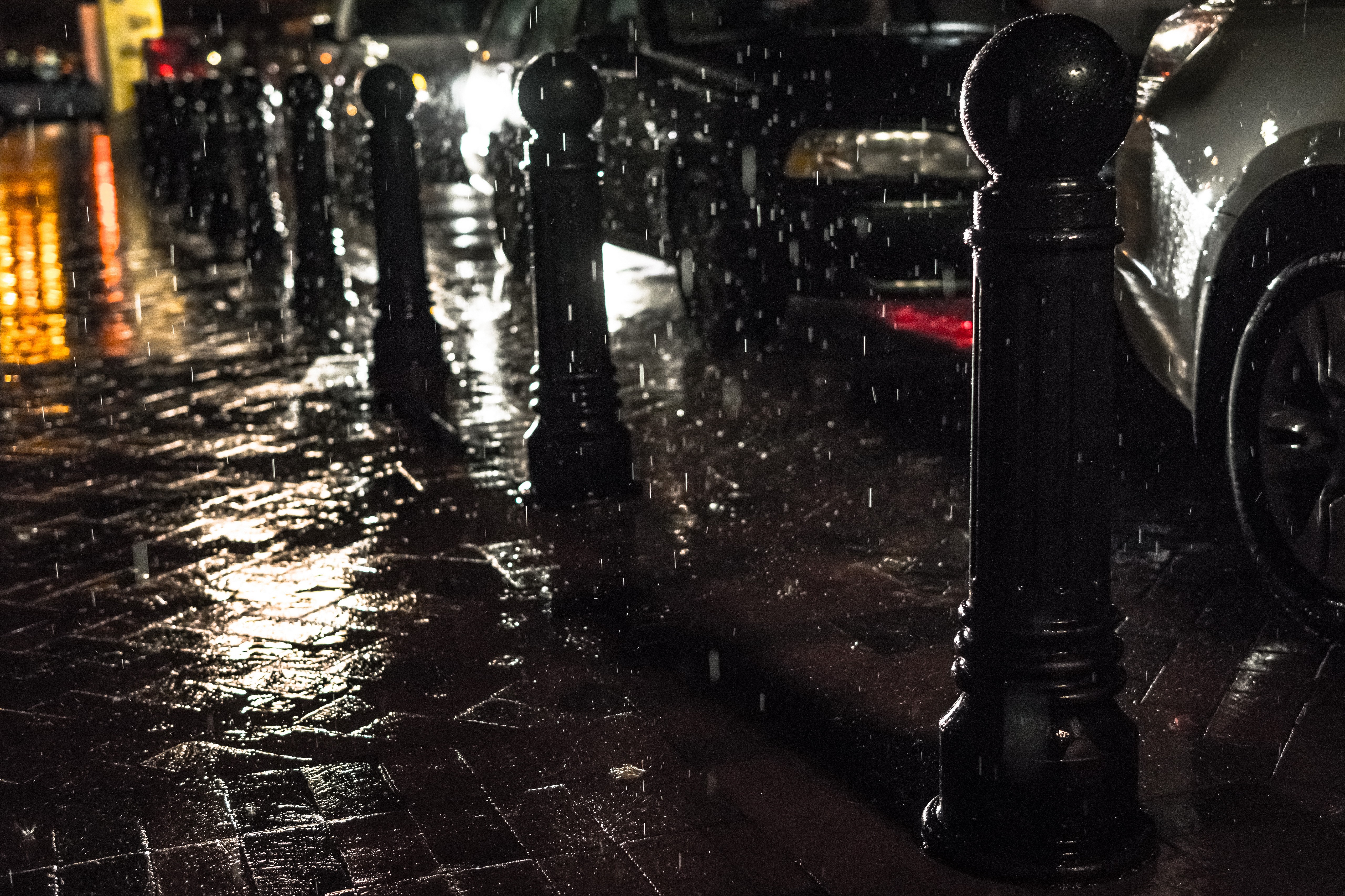 Rainy city street at night with cars and bollards HD Wallpaper