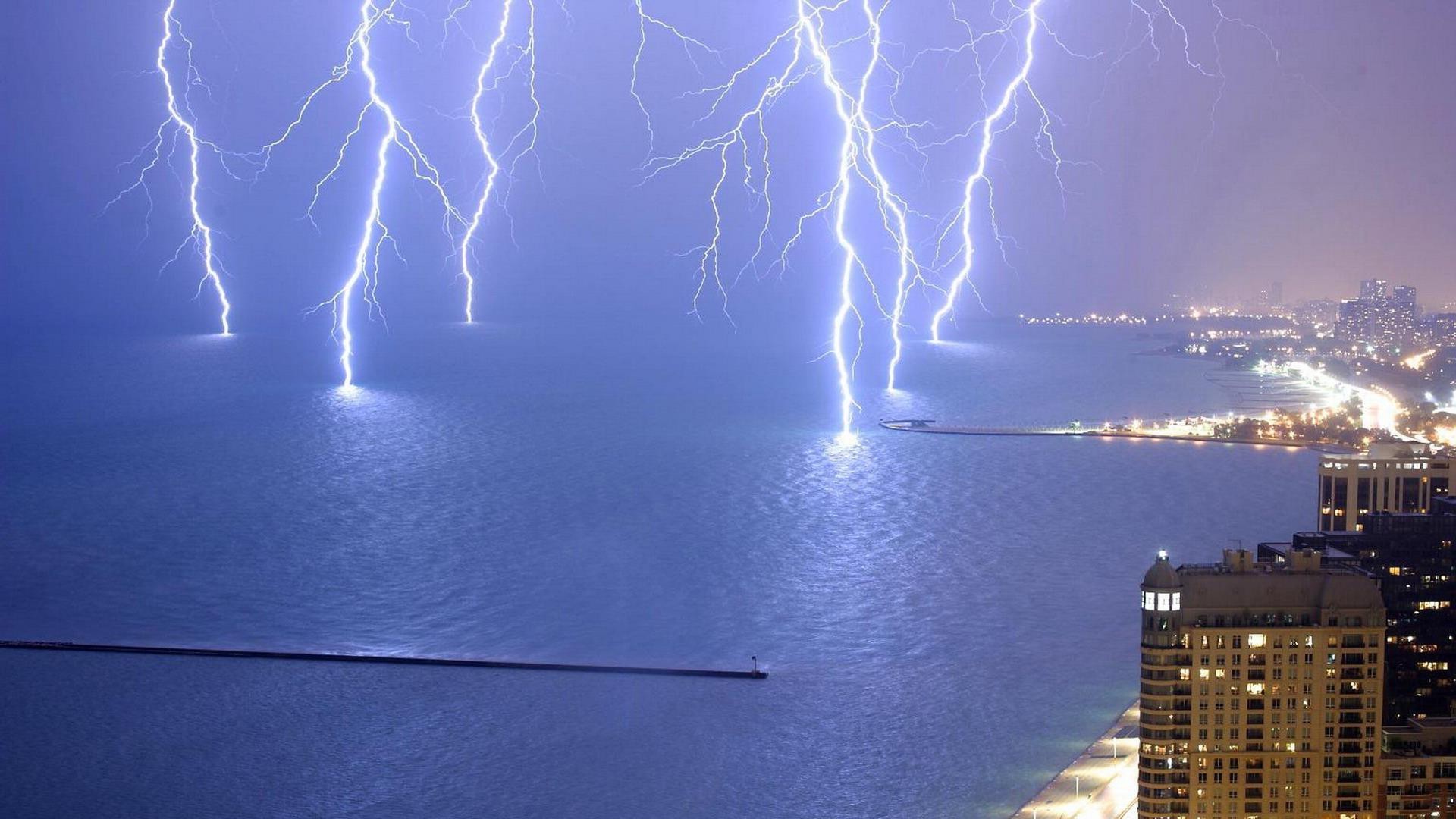 Lightning strikes over a city and sea at night HD Wallpaper
