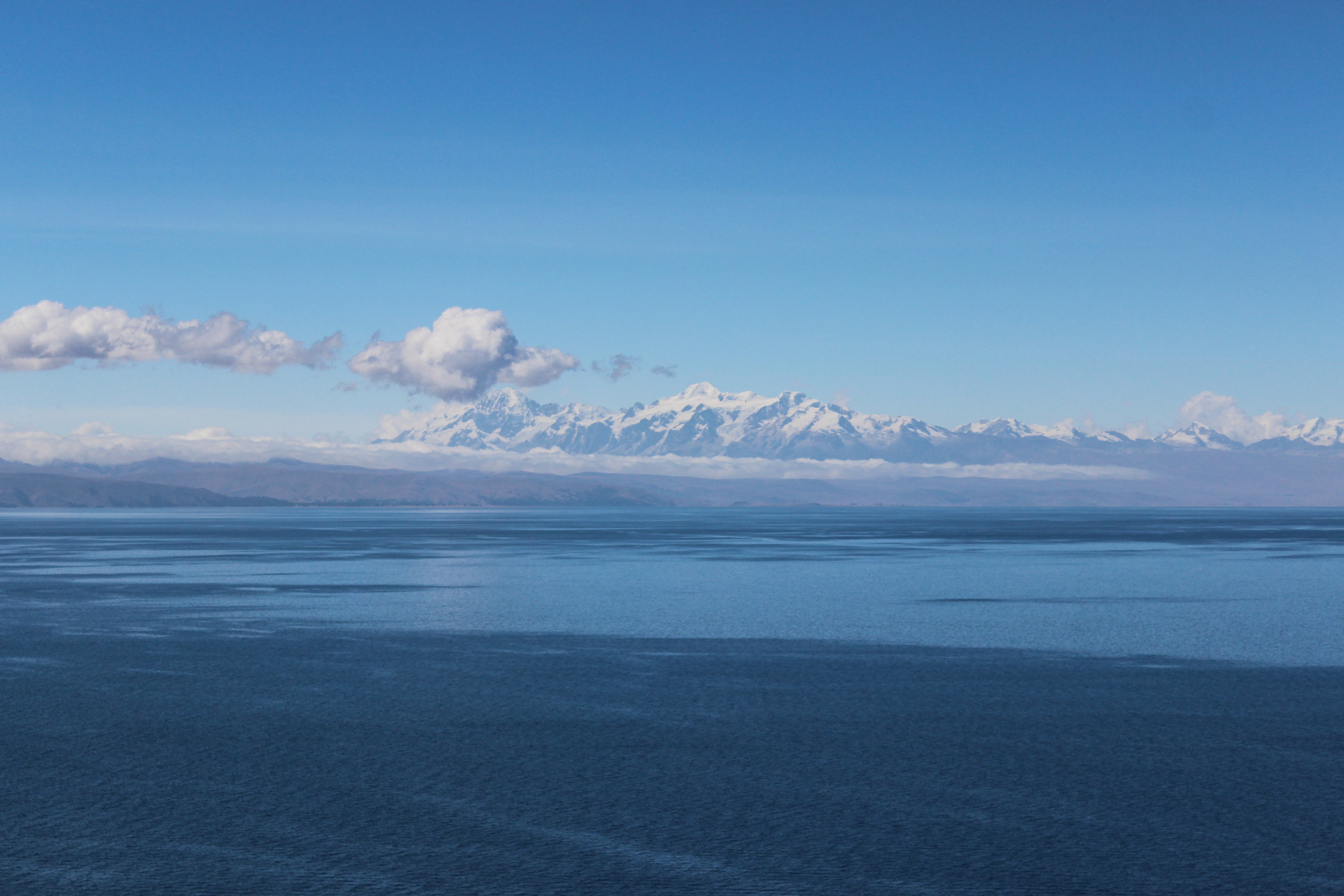 Lake Titicaca with snow-capped mountains under a clear blue sky HD Wallpaper