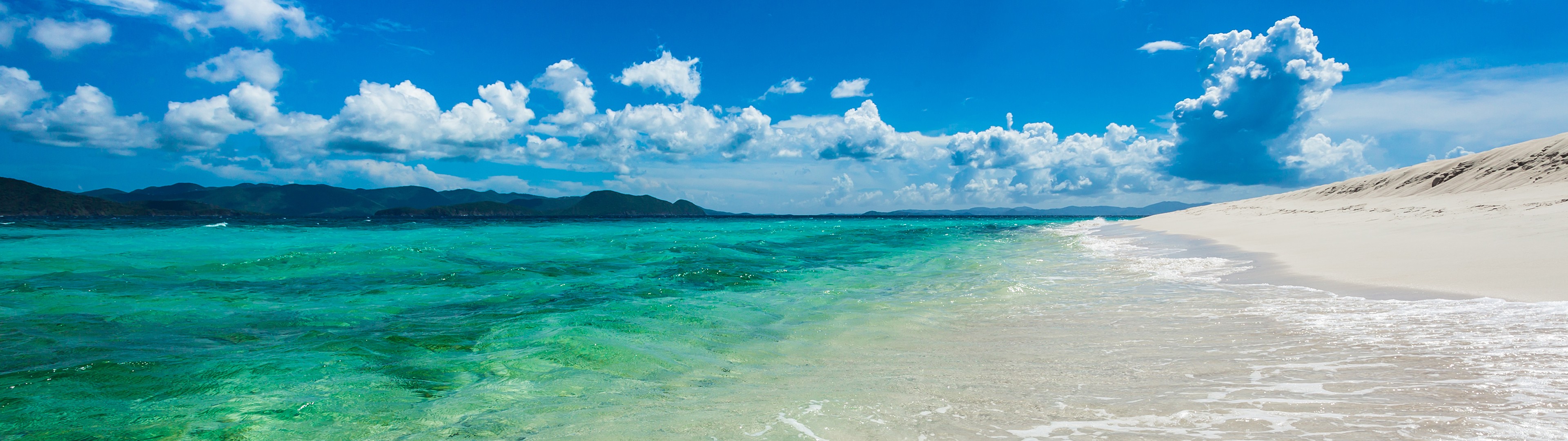 Turquoise ocean waves on a white sand beach under a blue sky with clouds HD Wallpaper