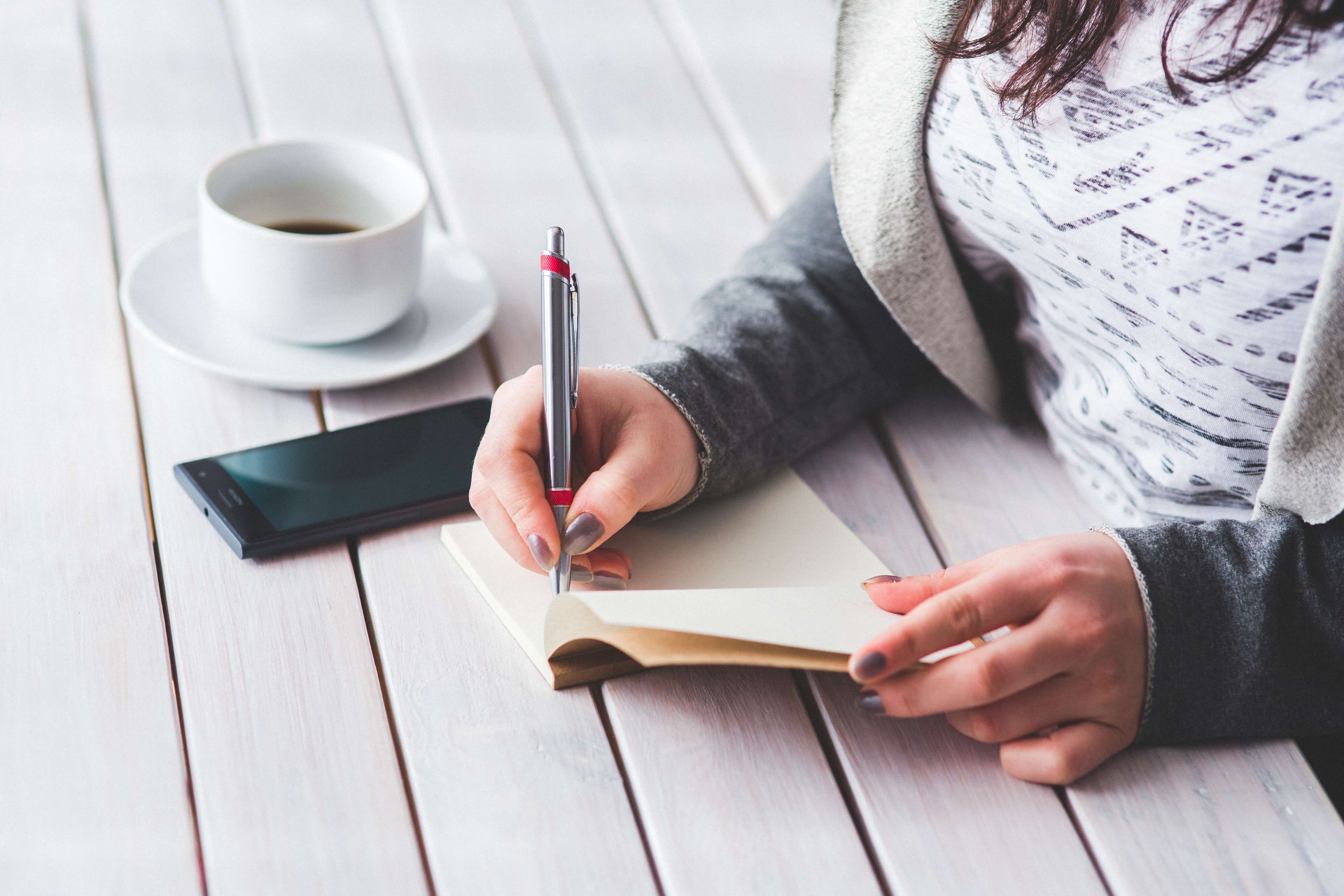 Woman writing in notebook with coffee and phone HD Wallpaper