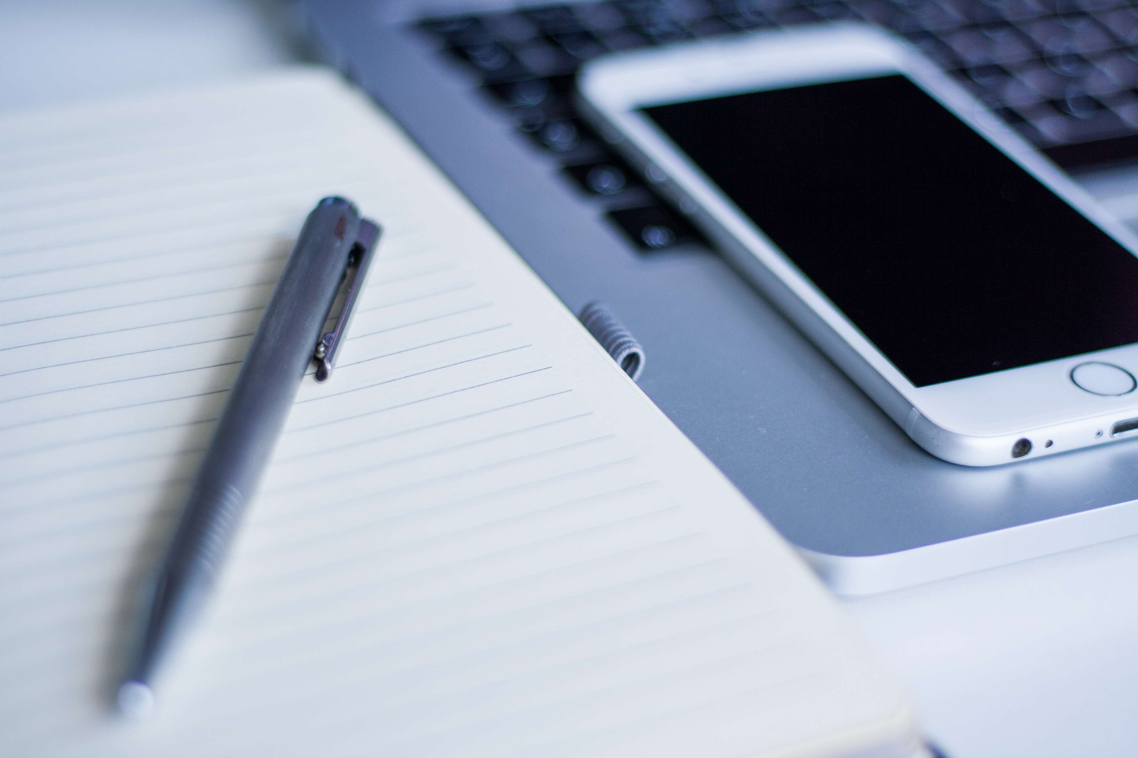 iPhone on laptop next to notebook and pen HD Wallpaper