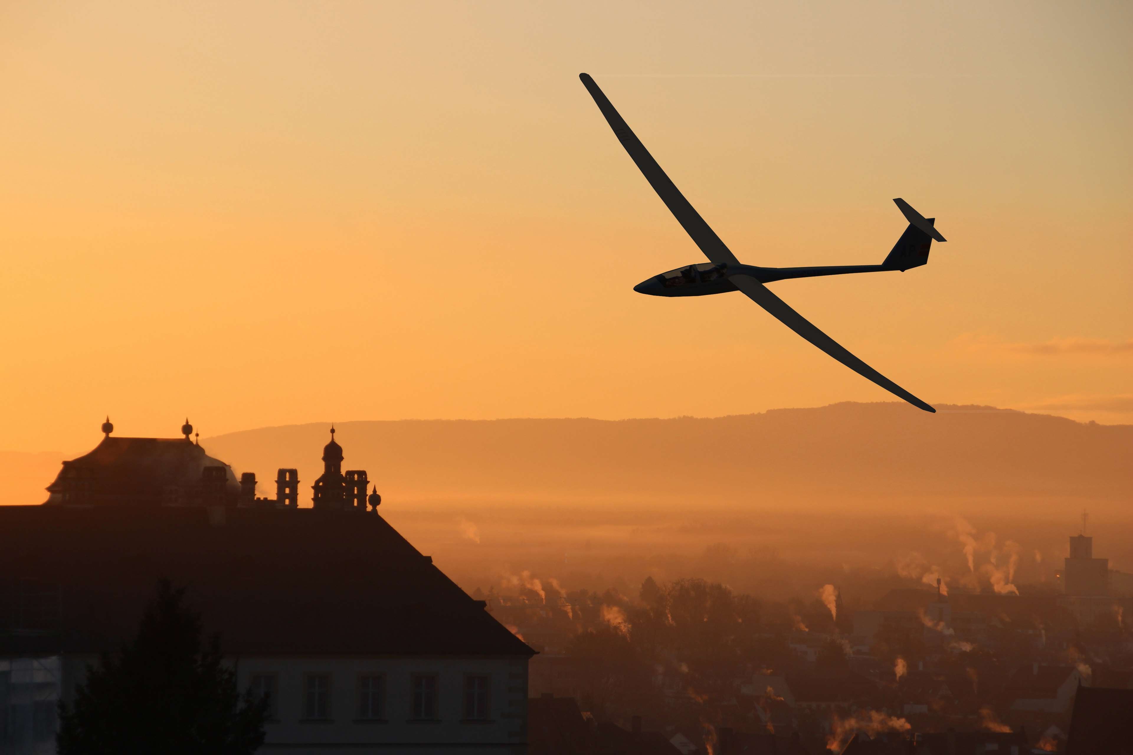 Glider flying over a city at sunrise HD Wallpaper