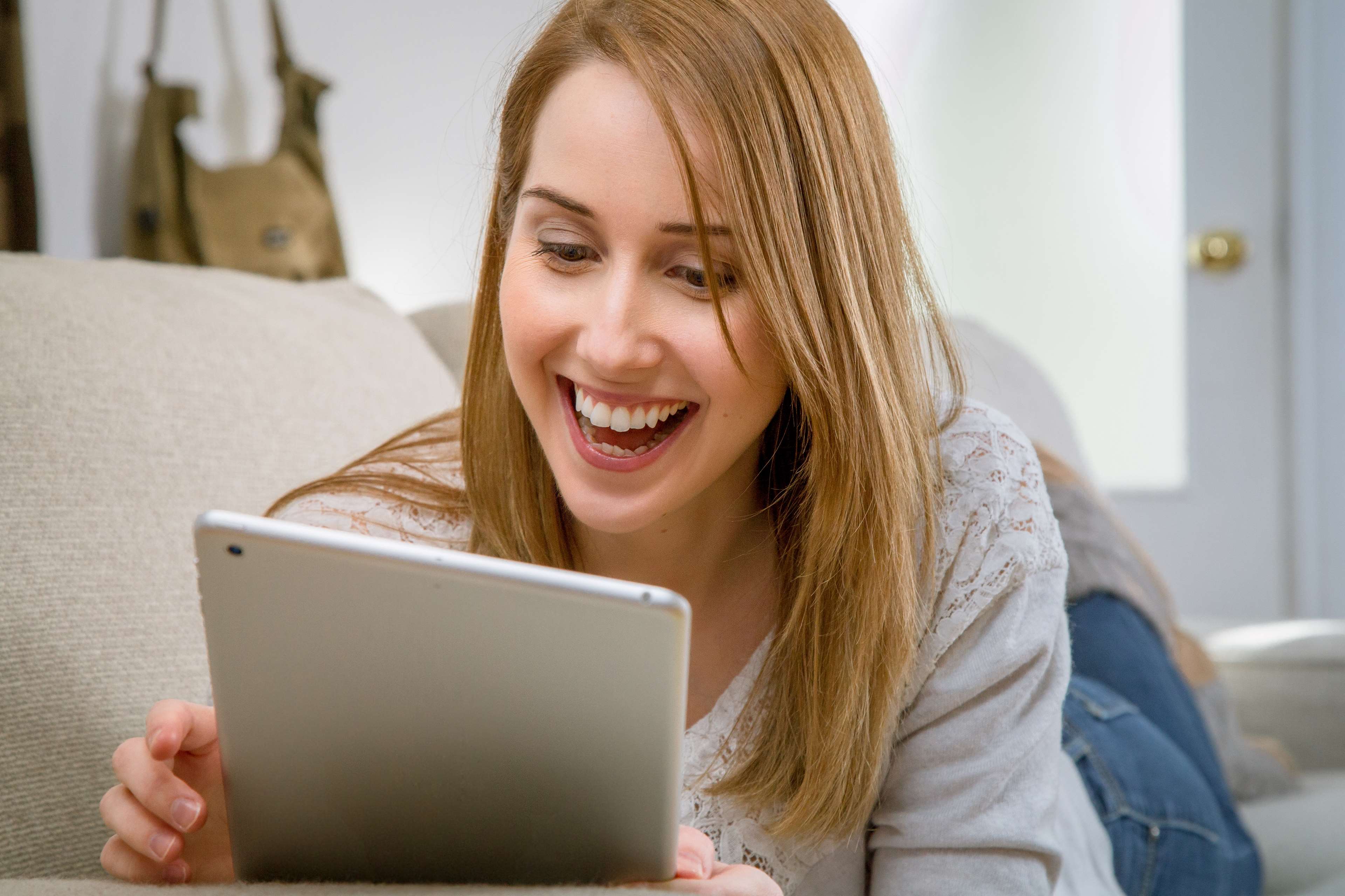 Woman laughing while looking at a tablet on a couch HD Wallpaper